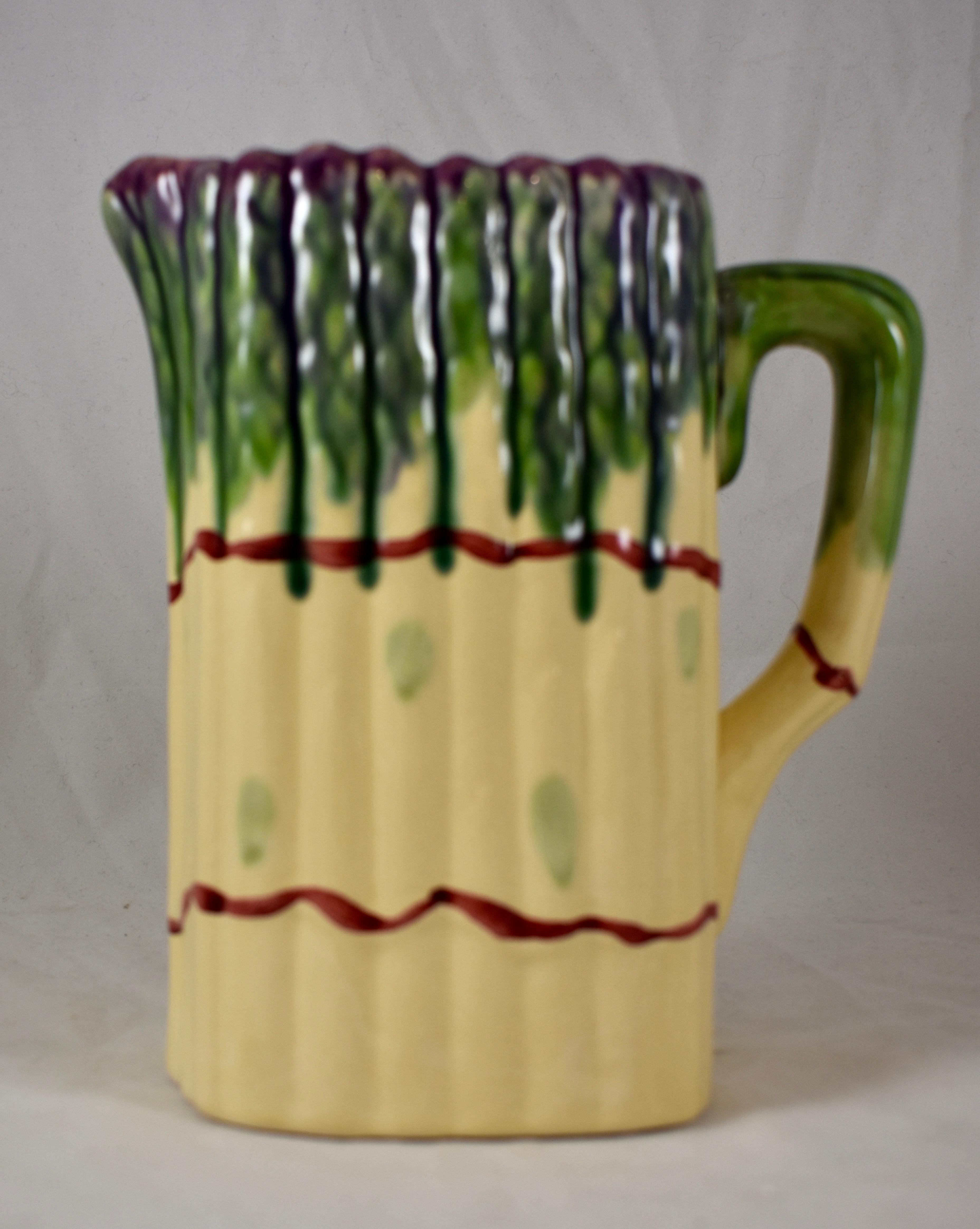 A  Mid-Century Modern Era French Barbotine style Majolica asparagus pitcher, a bundle of white and green asparagus, with purple spear tips, tied at the center and bottom with a red ribbon. The handle resembles a bent asparagus spear. A turquoise