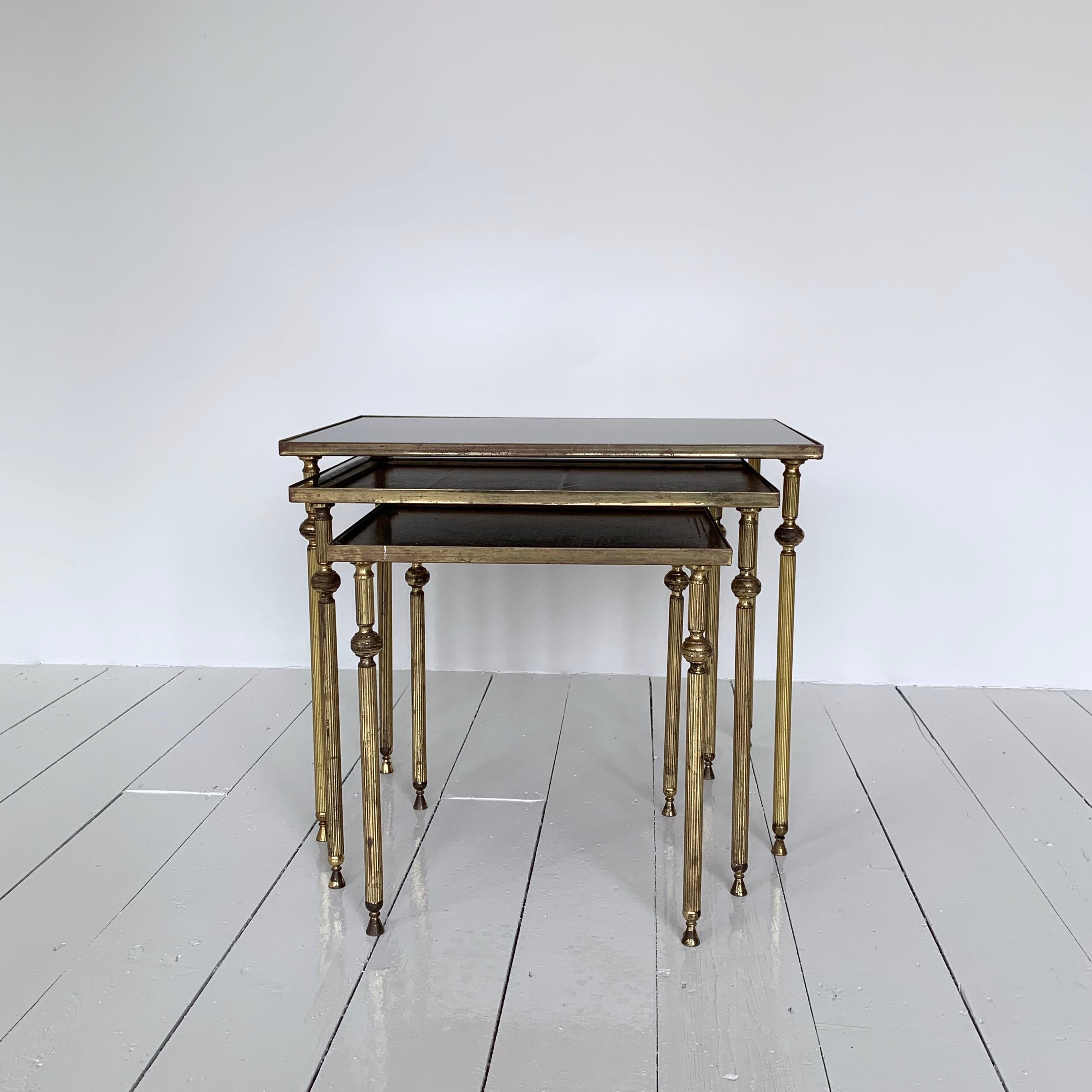 A nest of three side tables made from cast brass with black tinted mirrored glass tops. In the style of Maison Baguès these tables originate from 1950s France. All three are in excellent condition. Slight ageing to the mirrored glass can be seen in
