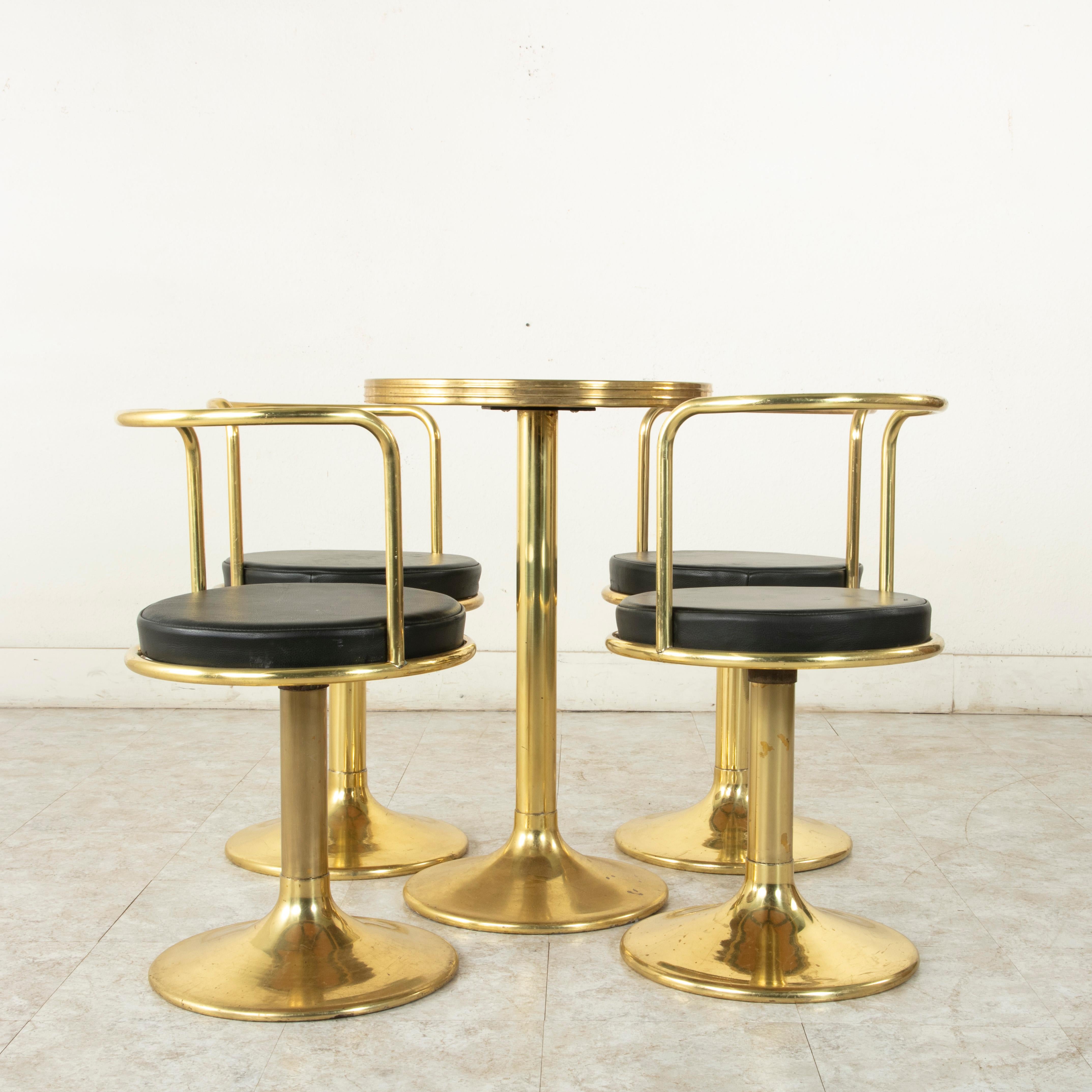 Originally used in the La Meuliere cabaret in Paris, this midcentury brass bistro set features a circular table with a black marble top and four chairs upholstered in black skai. The set rests on footed bases that gently slope outward. Its chairs