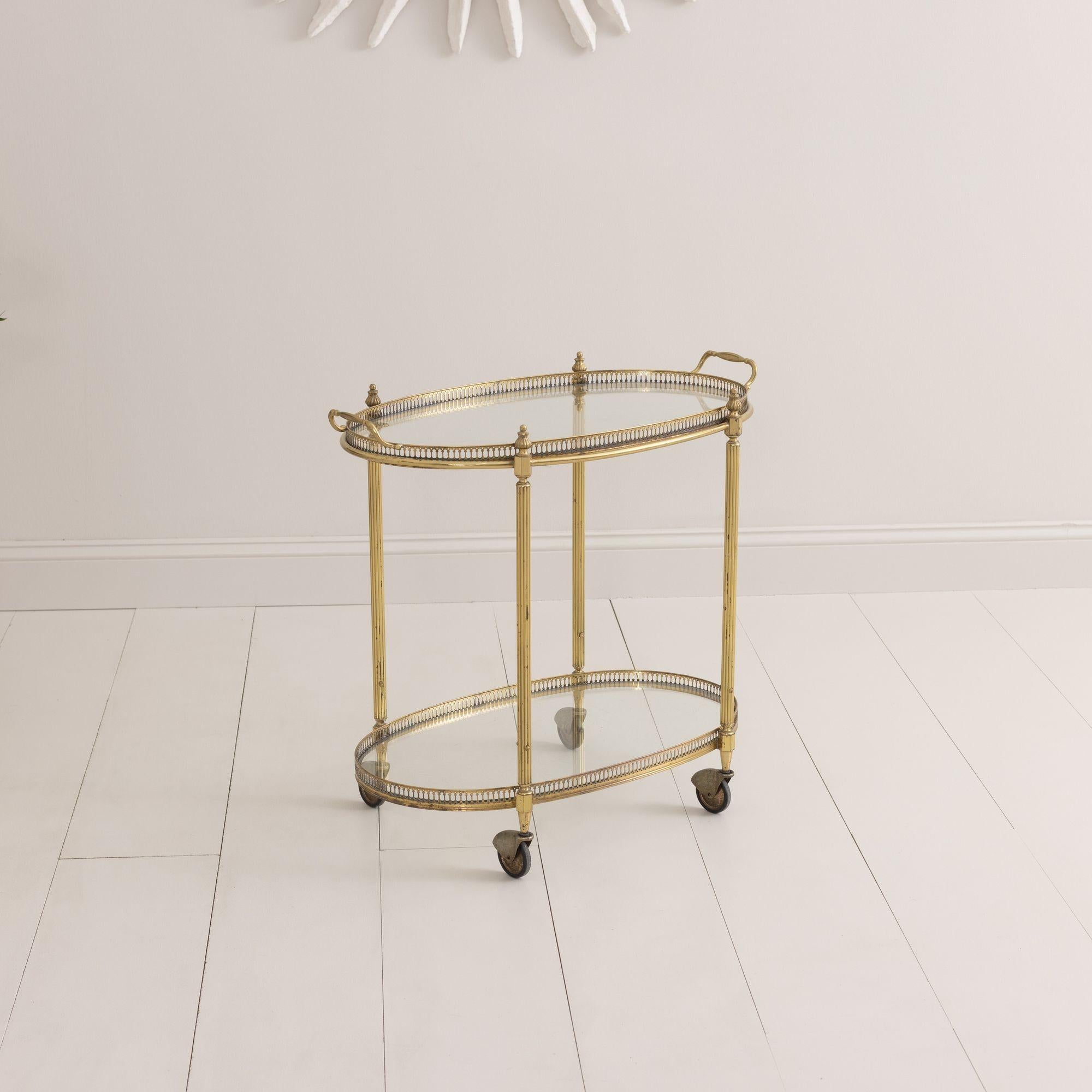 Vintage French brass serving trolly or bar cart with original castor wheels found in Paris, circa 1960.  Two-tiered glass with nicely patinated, pierced gallery to the top and bottom.  The top tray has handles and is removable.  Lovely round and