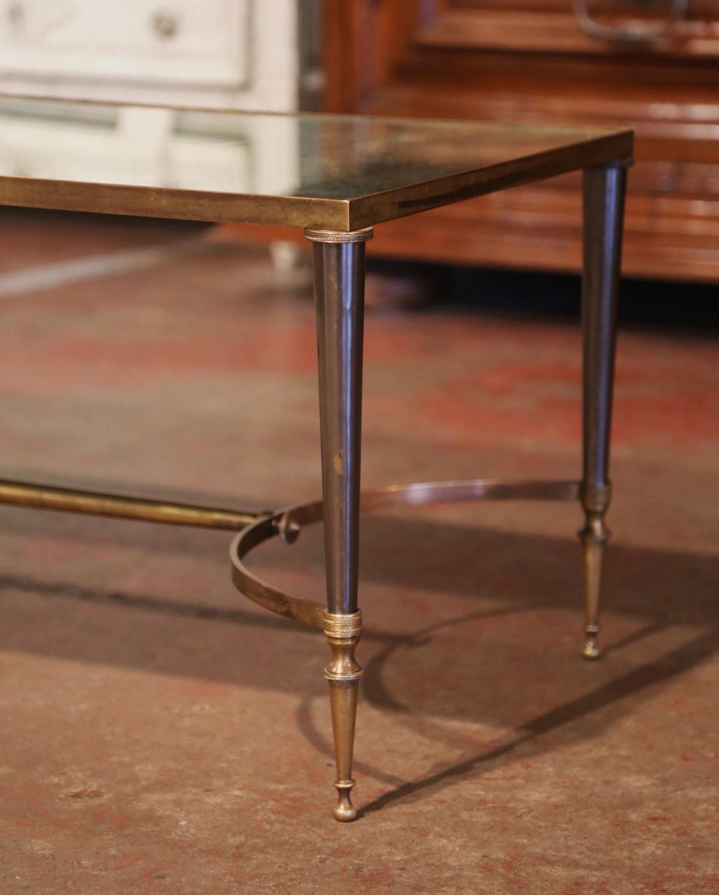 This elegant and slender cocktail table was crafted in France by Maison Baguès circa 1960; the table stands on four cast bronze tapered legs embellished with ring decor, over an arched bottom stretcher dressed with end finials. The surface is