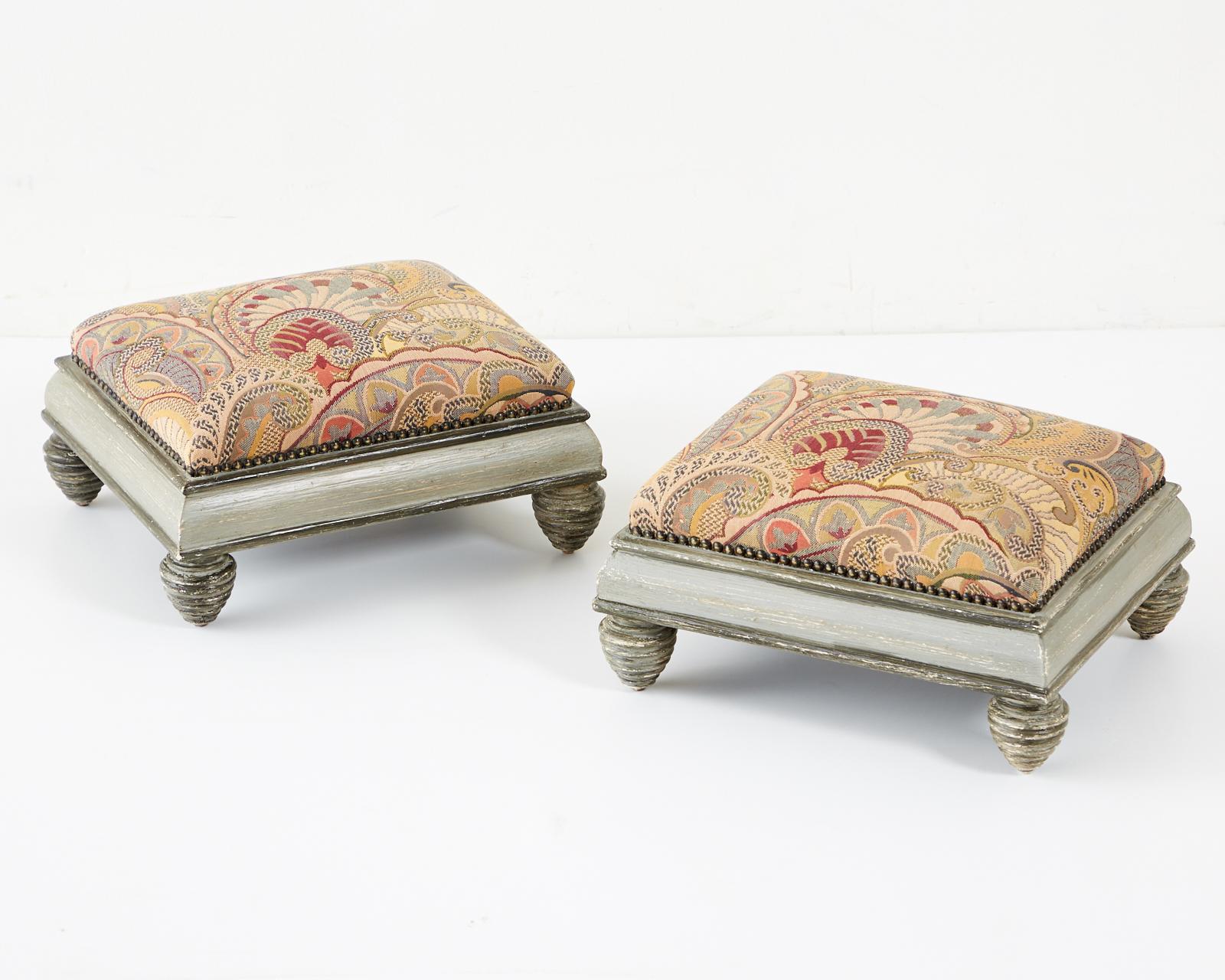 Rare pair of French Mid-Century Modern footstools by Brunschwig and Fils. Beautifully crafted near square frames with a lacquered gray two-tone finish. The decorative arts style fabric has a paisley motif and is bordered by brass tack nailheads. The