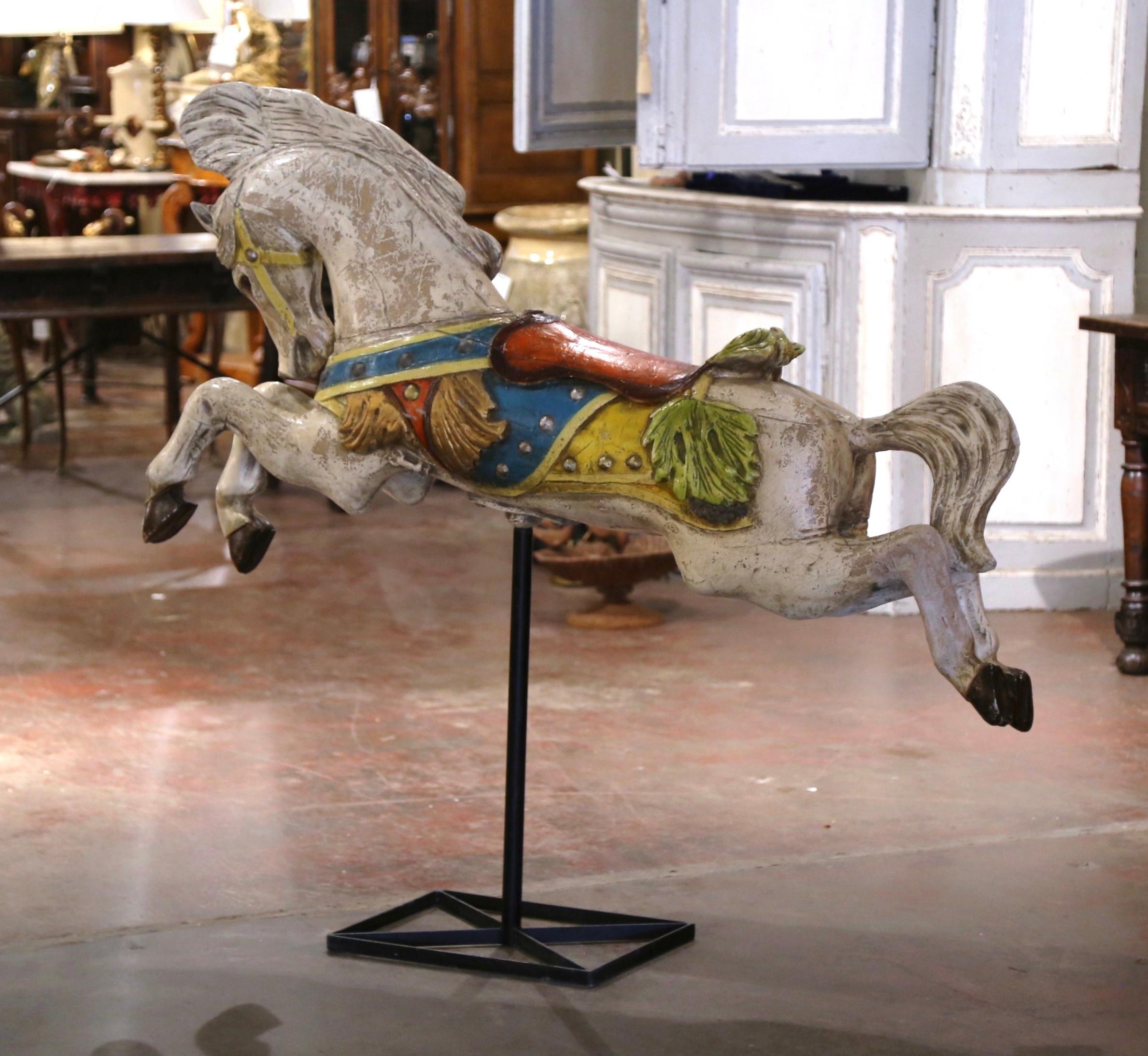 Crafted in France, circa 1960, this large, hand carved sculpture sits on an attached square iron base and depicts a colorful hand-painted horse figure. The horse features a flowing mane and a dynamic pose as if in mid-gallop, evoking a sense of