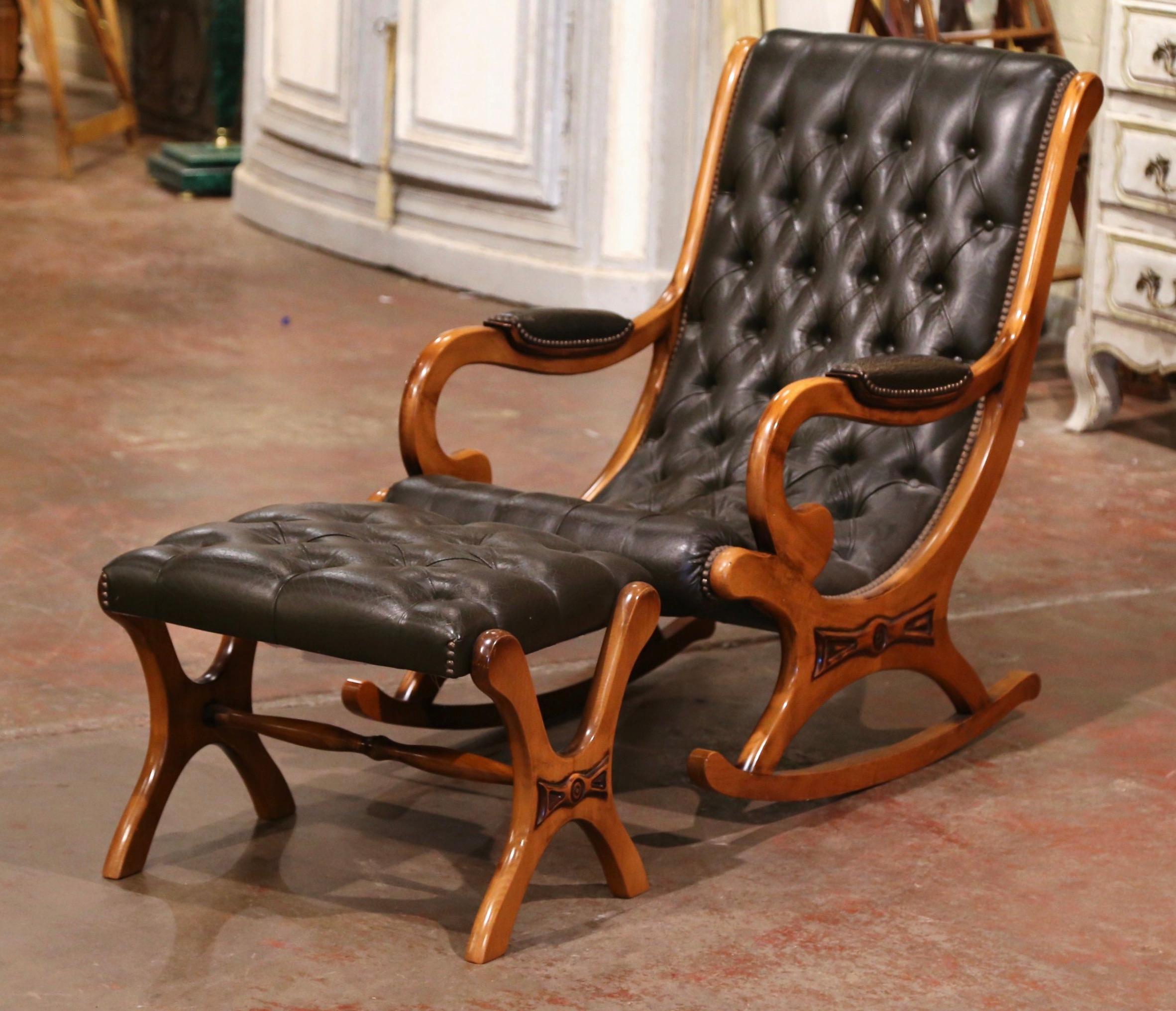 Crafted in France circa 1960, the armchair stands on rocking legs and features elegant lines with a rounded back, curved armrests over a carved applique medallion. Both club chair and stool are upholstered with a black tufted leather and embellished