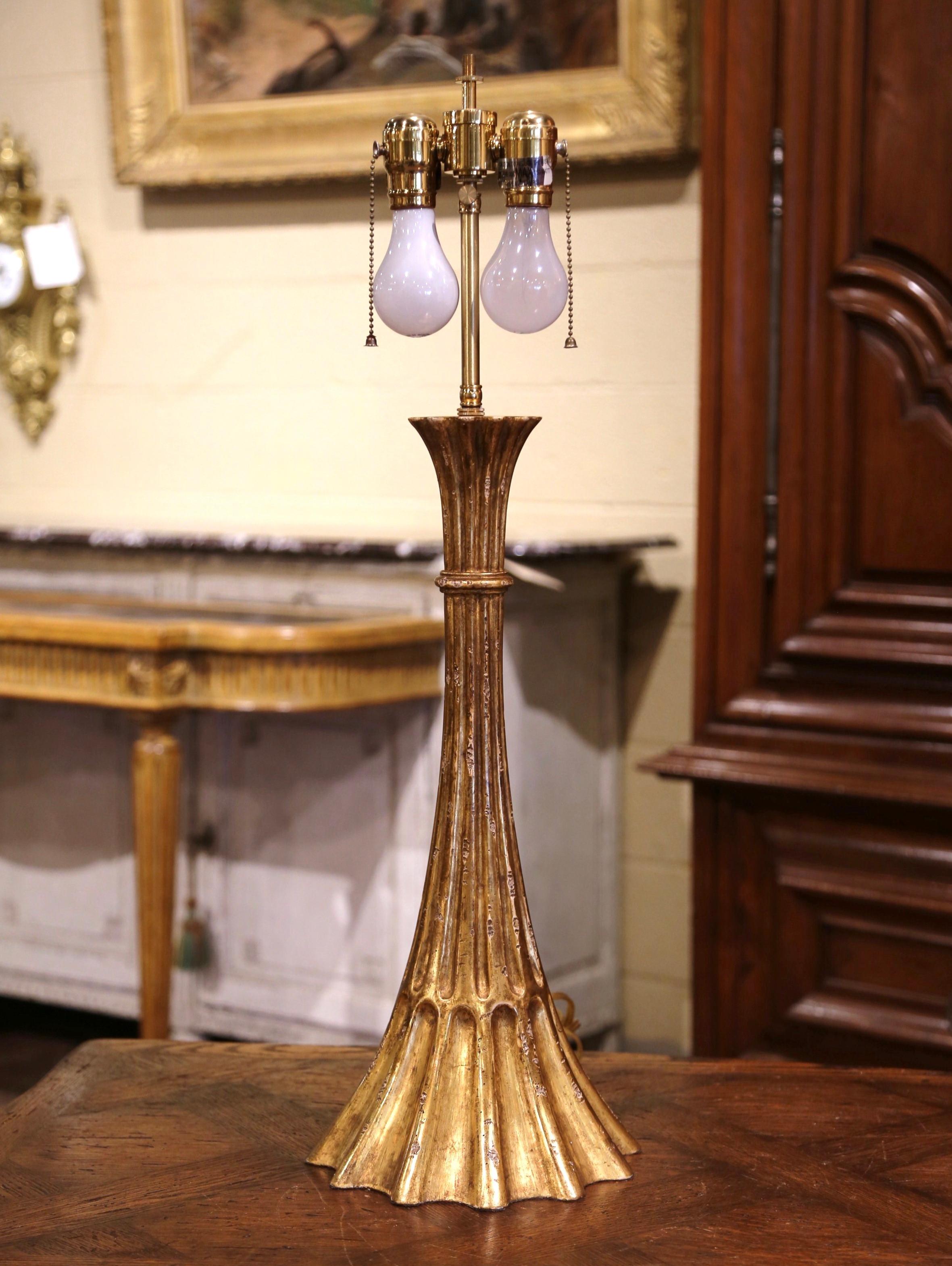 Hand carved in France circa 1960, the antique lamp base features a cone shape with spline decor, and adorns a beautiful gilt finish; it has a custom creamy shade with gold trim. The elegant table lamp is in excellent condition with dual lights, and