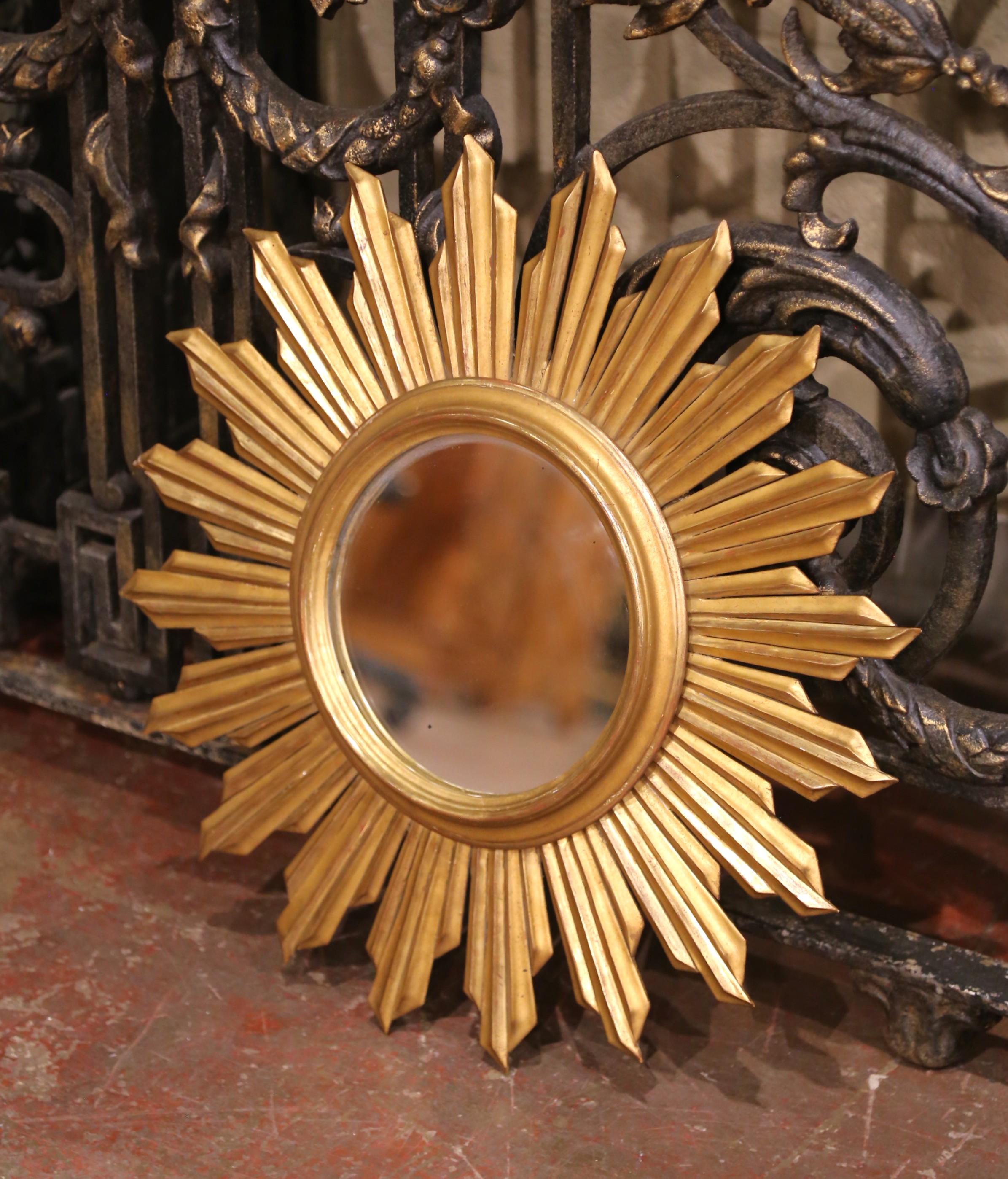 Radiating timeless charm, this mid-century French sunburst mirror is crafted from hand-carved wood with a warm gilt finish. Measuring 21.5 inches in diameter, the piece features sharply faceted rays in alternating lengths that create striking visual