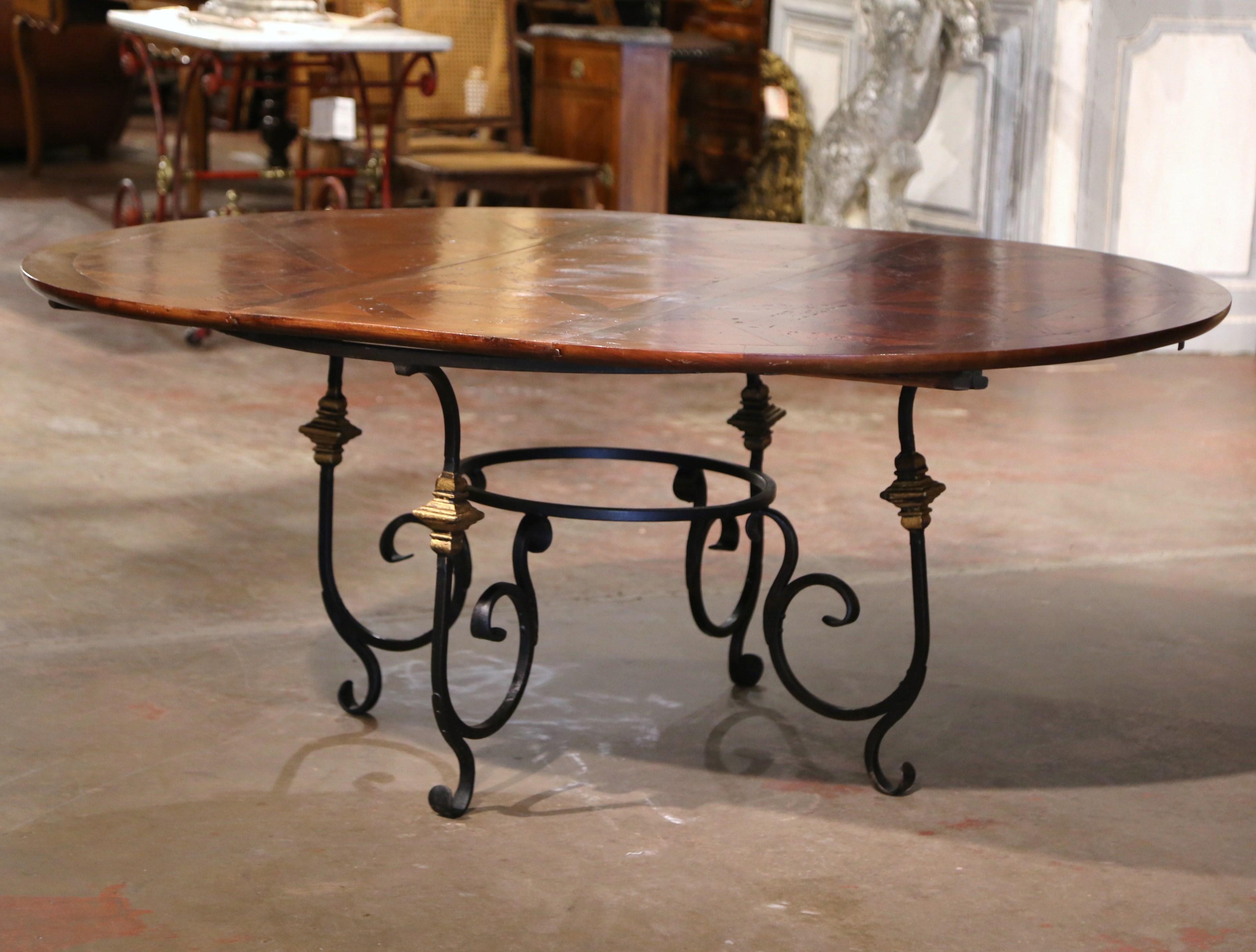 Crafted in Lyon, France circa 1950, the walnut table stands on forged wrought iron base with elegant scrolled legs and connected with a round stretcher. The circular walnut top showcases old timber planks set in a parquet geometric pattern. The top