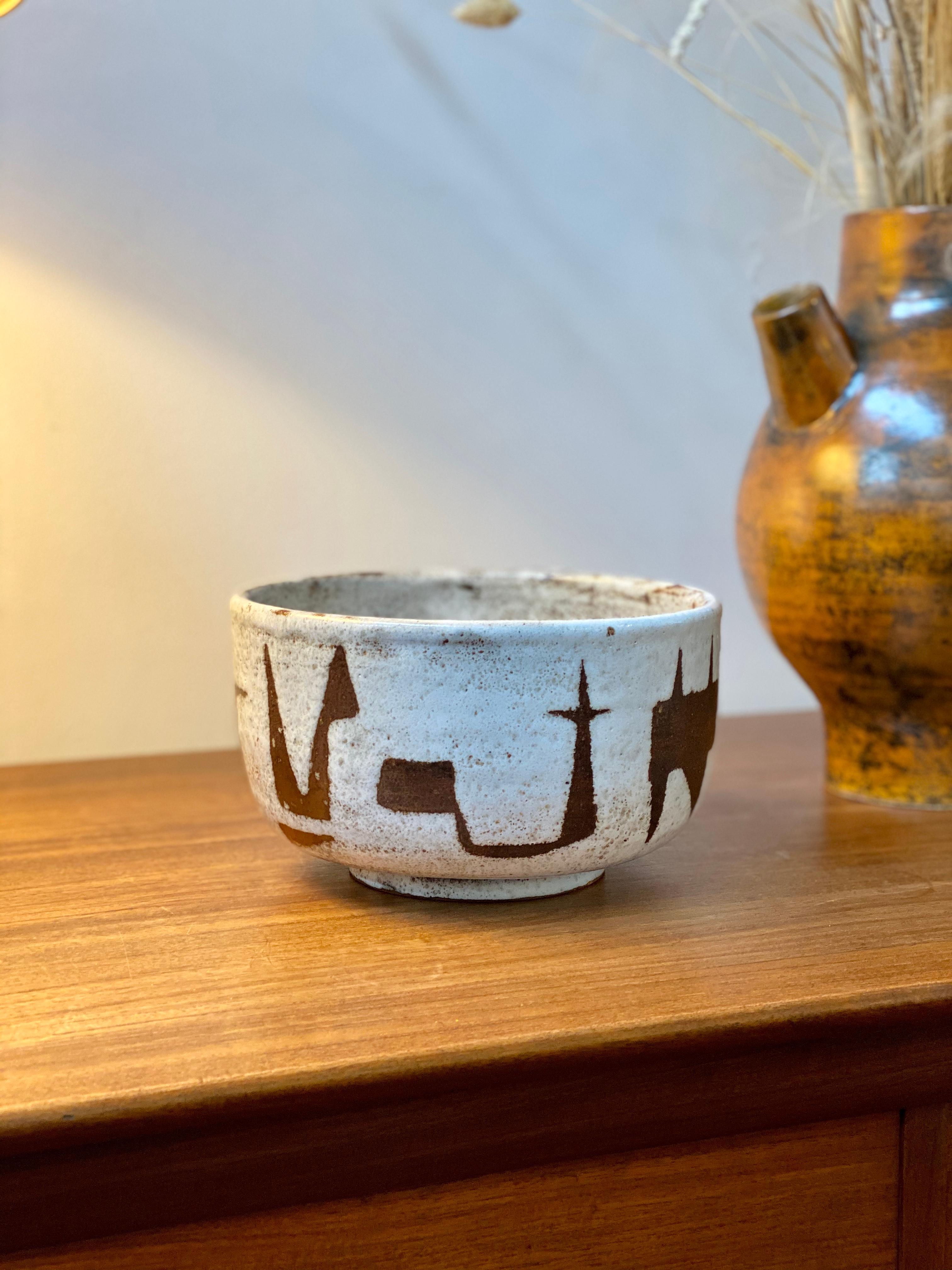 Midcentury French ceramic bowl by Jean Rivier (circa 1960s). A stunning, modern design earthenware bowl in off-white with chocolate brown zoomorphic shapes. The figures are reminiscent of Prehistoric African art and surround the exterior of the