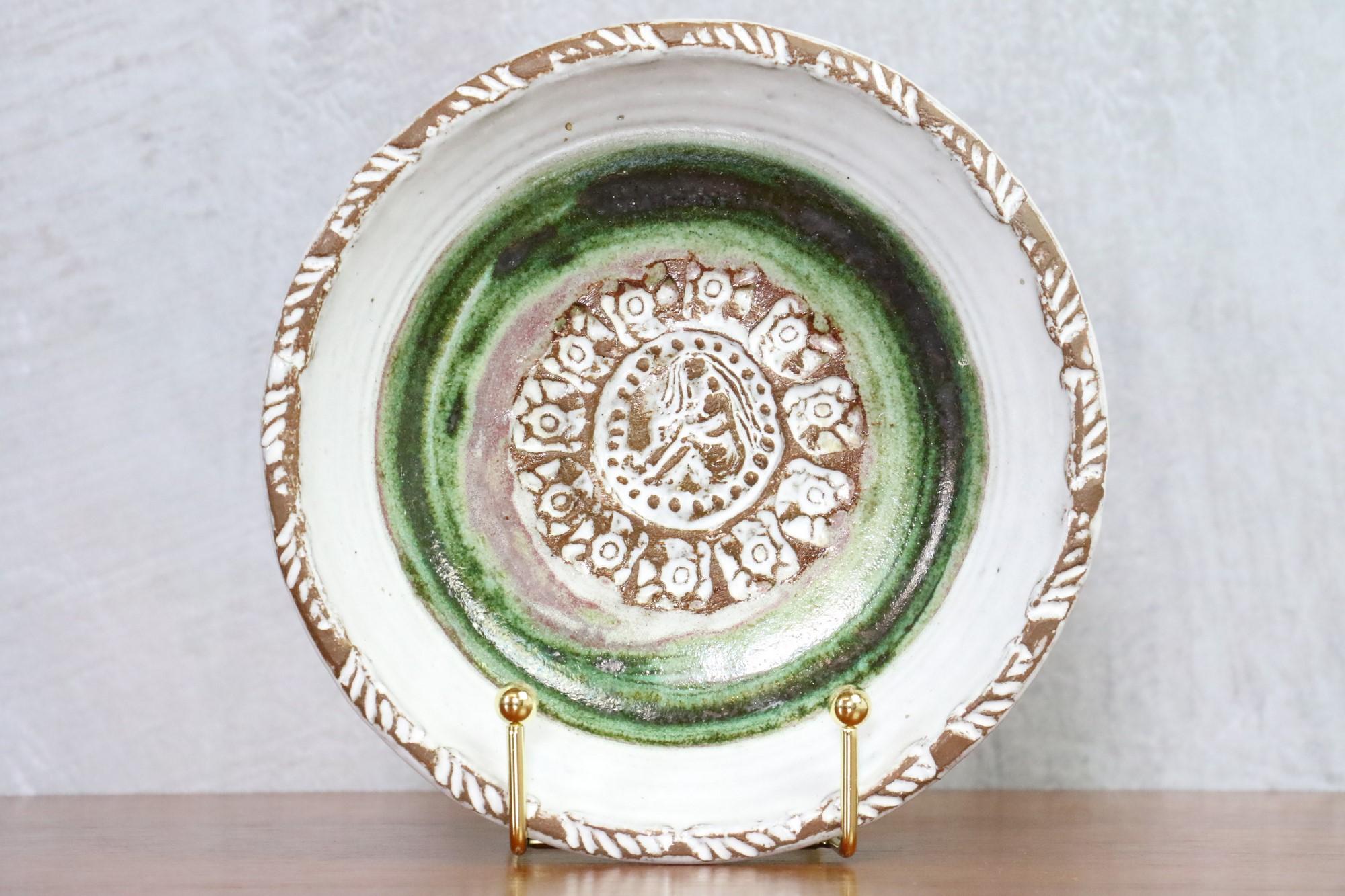Mid-century French Ceramic decorative plate by Albert Thiry - 1960s 

Very nice green and brown decorative plate. In the center is a setting of a seated woman surrounded by abstract motifs.
The colors and the work of the chamotte clay are typical
