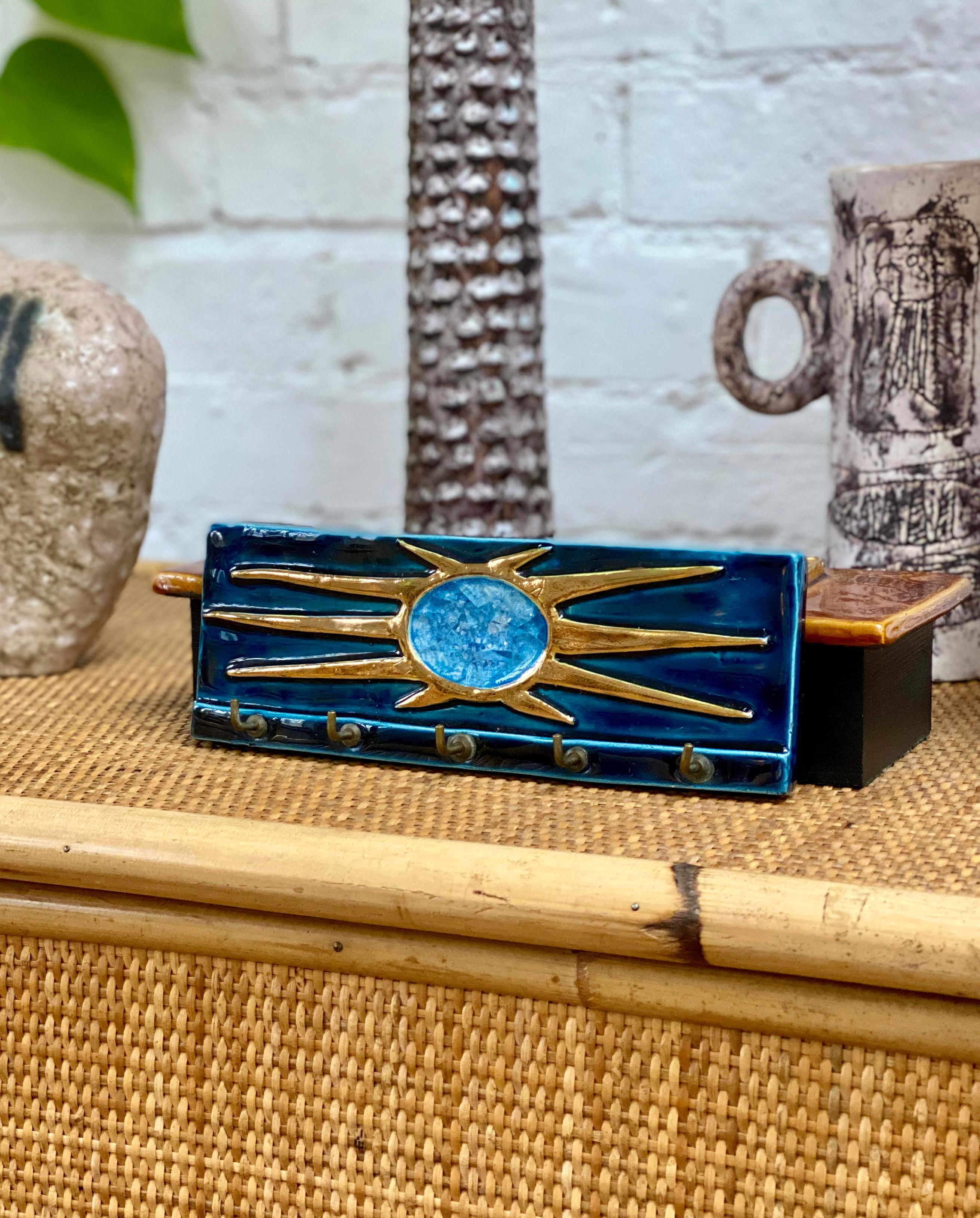 A delightful, decorative midcentury French key or accessory holder in a lustrous, azure blue enamel base, topped by a decorated sun motif in gold crackle with cut fragments of colorful enameled glass in the centre. This piece is in good vintage