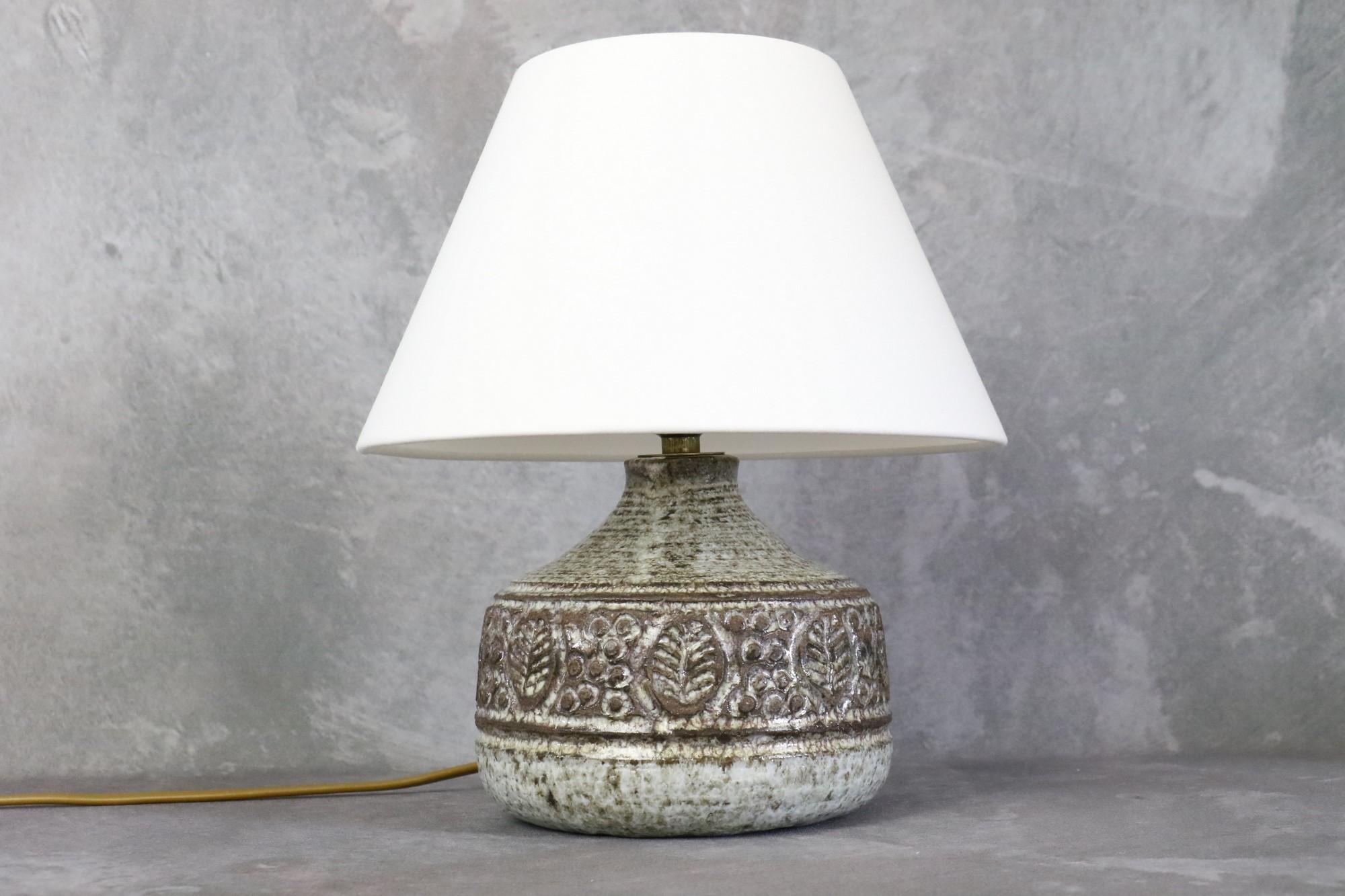 Mid-century French ceramic lamp by Marcel Giraud - Vallauris - 1960s.

There is a beautiful contrast between the use of a dark clay and the milky white glaze that gives relief to the nature-inspired motifs.
It is a beautiful object both raw and