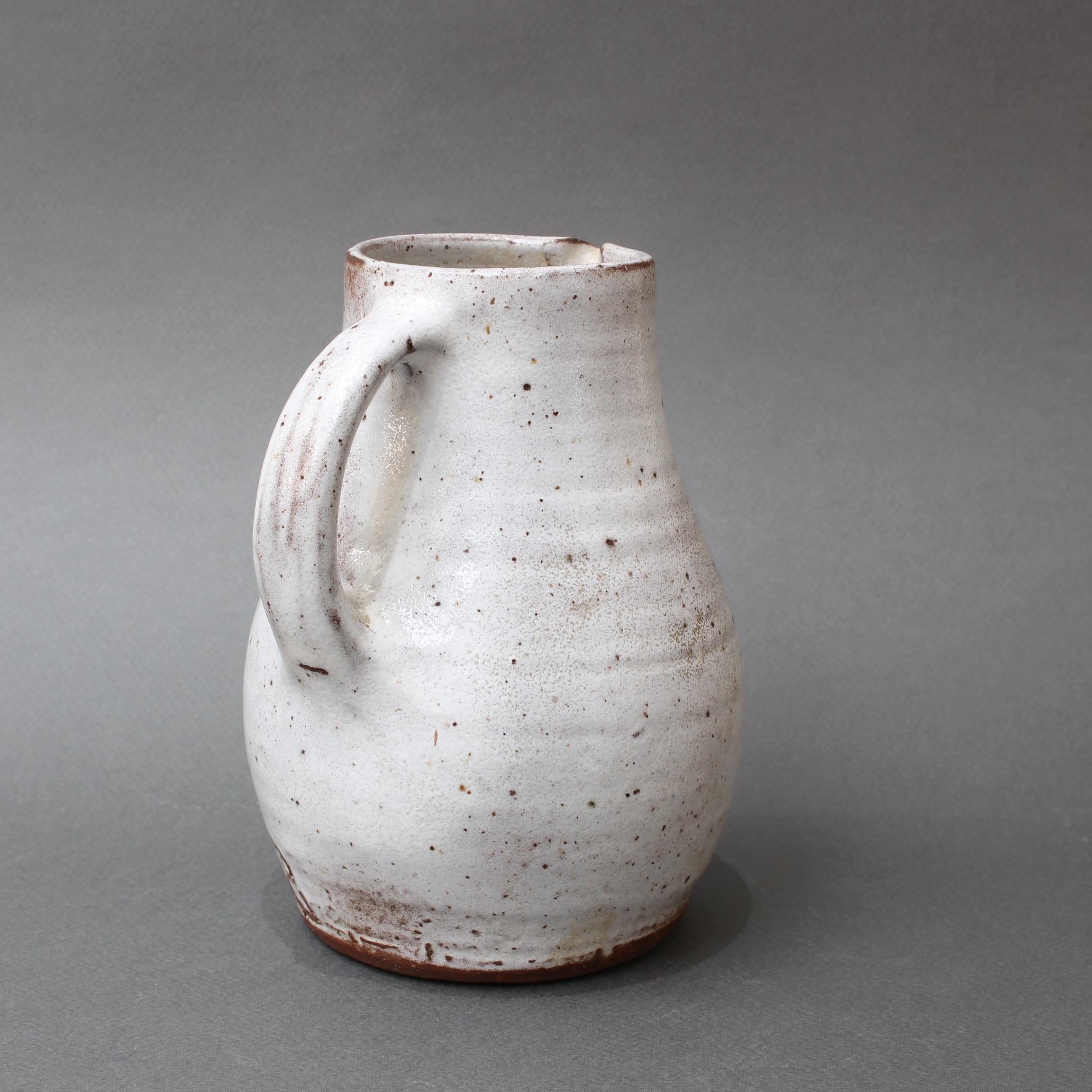 Mid-Century French ceramic pitcher by Jeanne & Norbert Pierlot (circa 1960s). With an off-white base and brown sandstone accents, this small, rustic pitcher with handle and spout is a delight. The glazed parts that are predominantly off-white are
