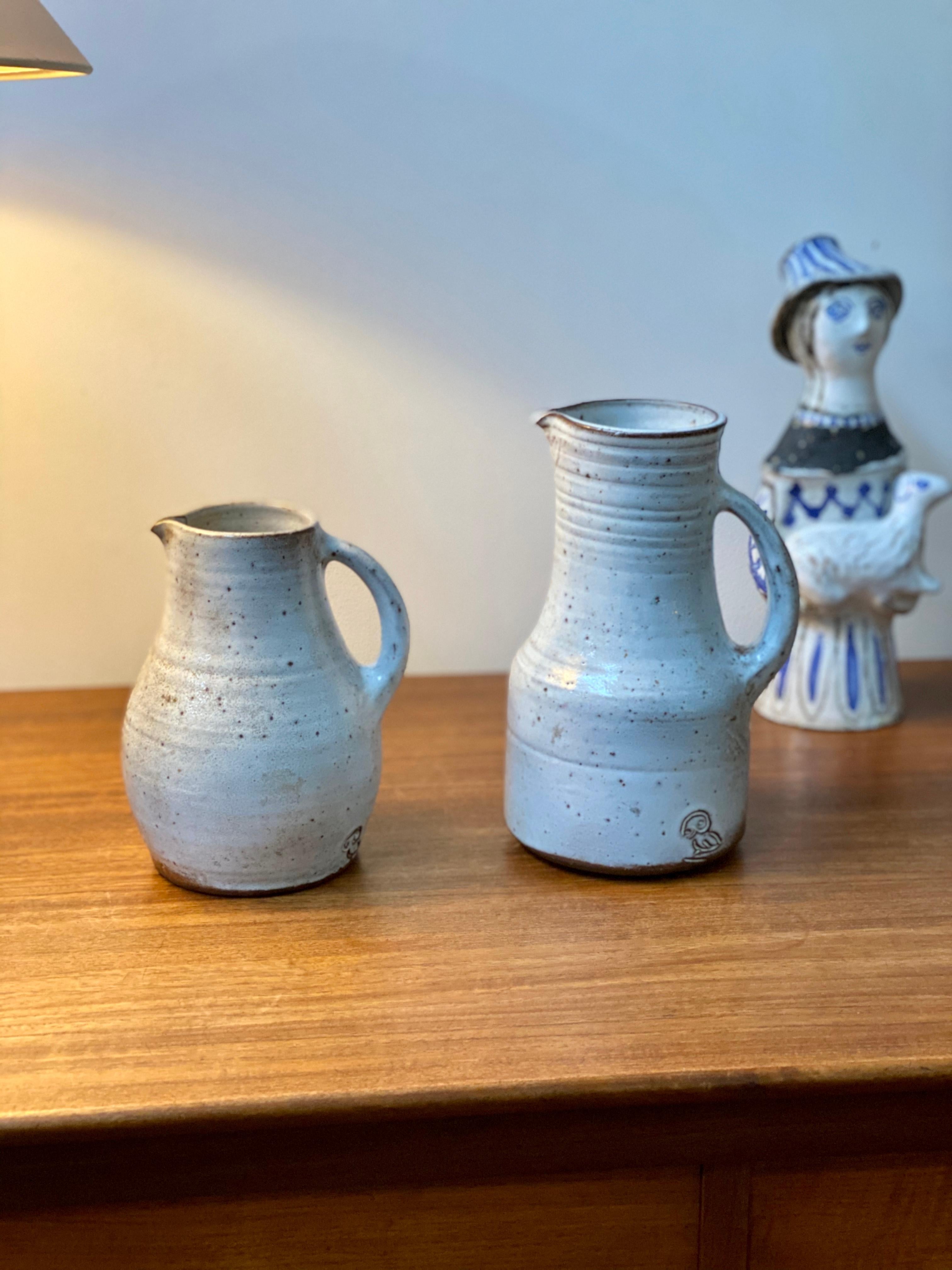 Midcentury French ceramic pitcher by Jeanne & Norbert Pierlot (circa 1960s). With an off-white base and brown sandstone accents, this rustic pitcher with handle and spout is a delight. The glazed parts that are predominantly off-white are lustrous