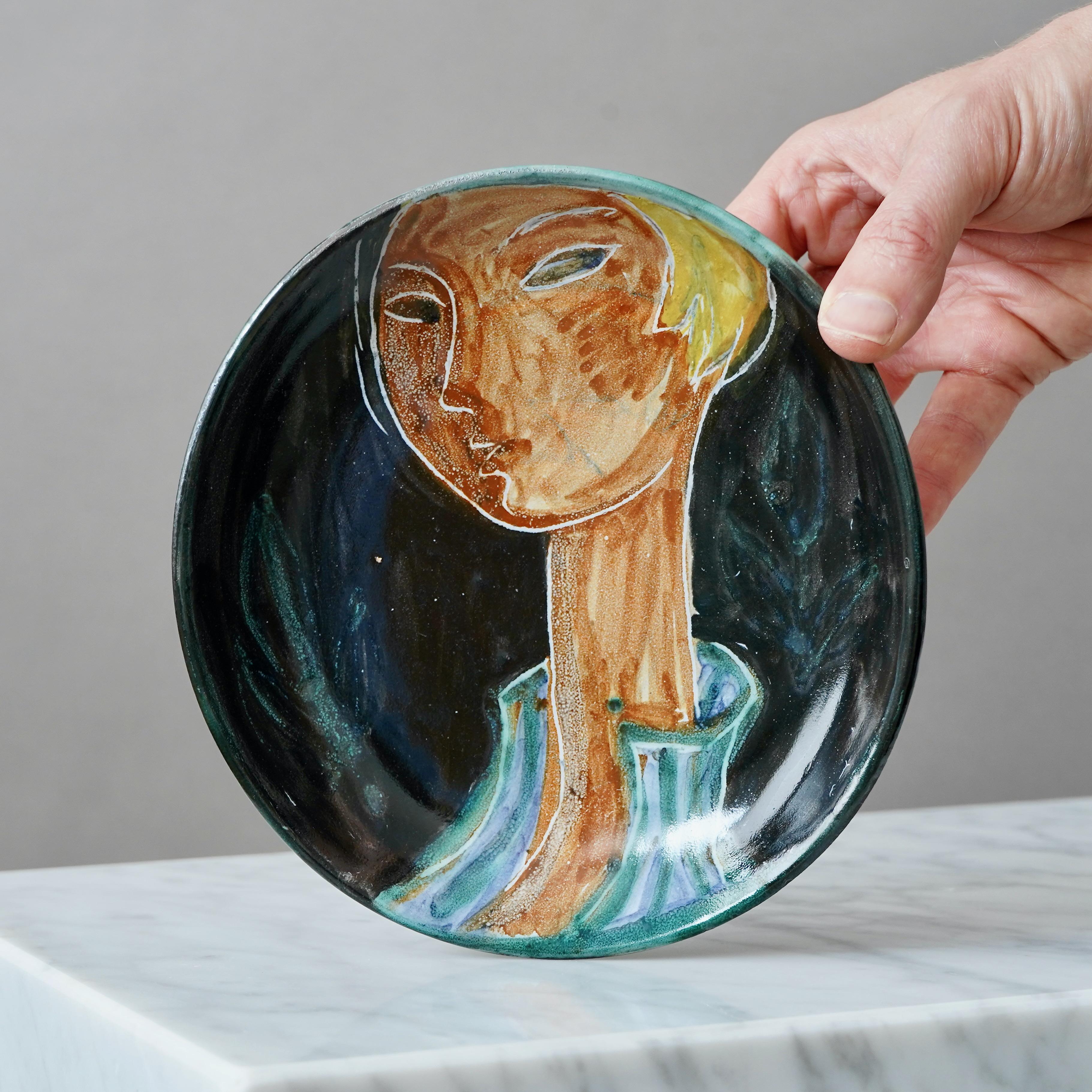 Plato de cerámica curvada francesa de mediados de siglo, pintado a mano con el rostro de una mujer con el pelo corto, por Ljuba Naumovitch en el Atelier du Grand Chêne, Vallauris (hacia los años 50). 

Gran condición.
Firmado y estampado en la parte