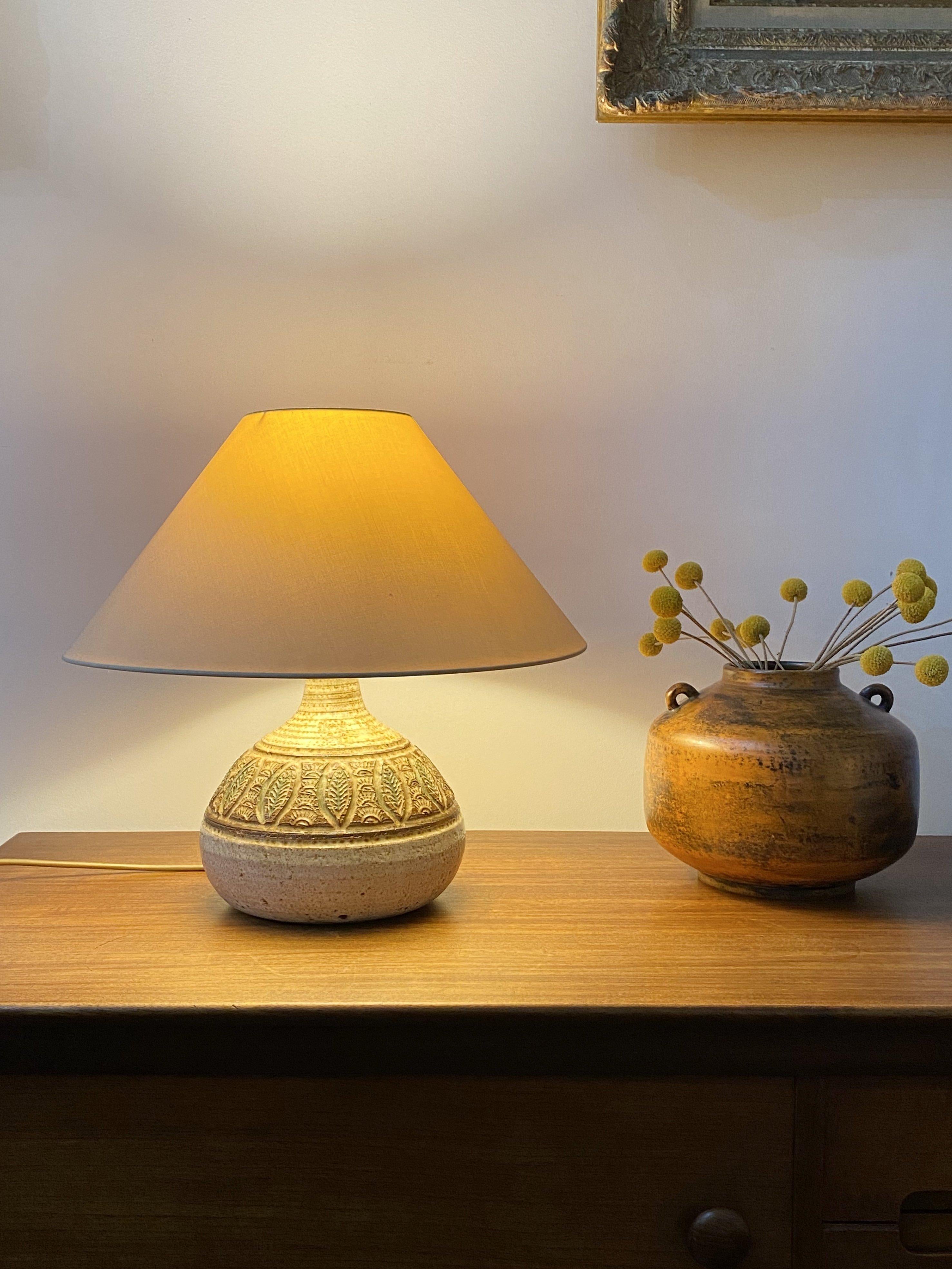 Midcentury ceramic glazed table lamp (circa 1960s) by Marcel Giraud, Vallauris, France. A piece with a graceful, rounded shape with wide centre in a muted chalk-colored base. This stunning lamp has a palm tree and leaf motif just above the centre