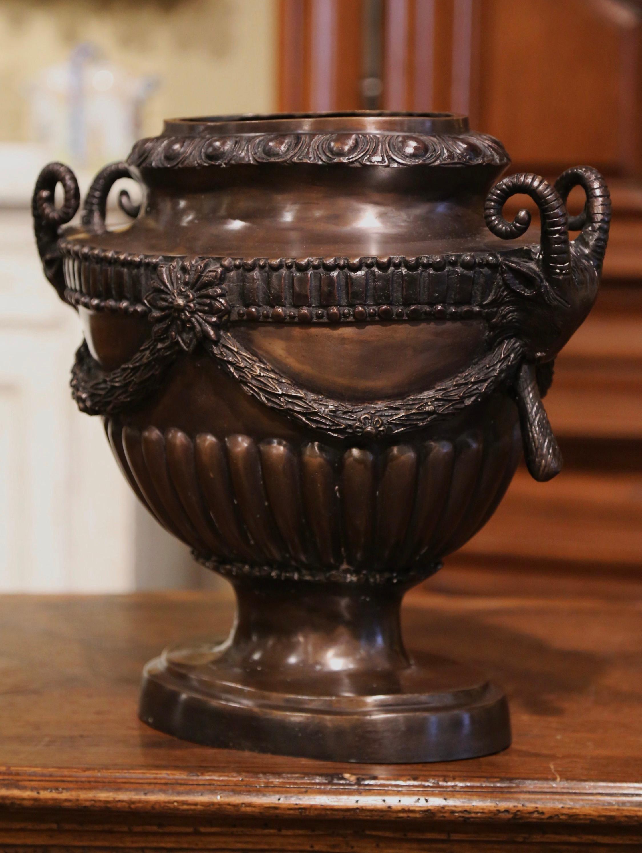 Crafted in France circa 1950 and oval in shape, this elegant Neo-classical bronze urn stands on a pedestal foot base; the vase is decorated with ram's head handles, swag motifs and laurel leaf festoons around the perimeter. The antique indoor or