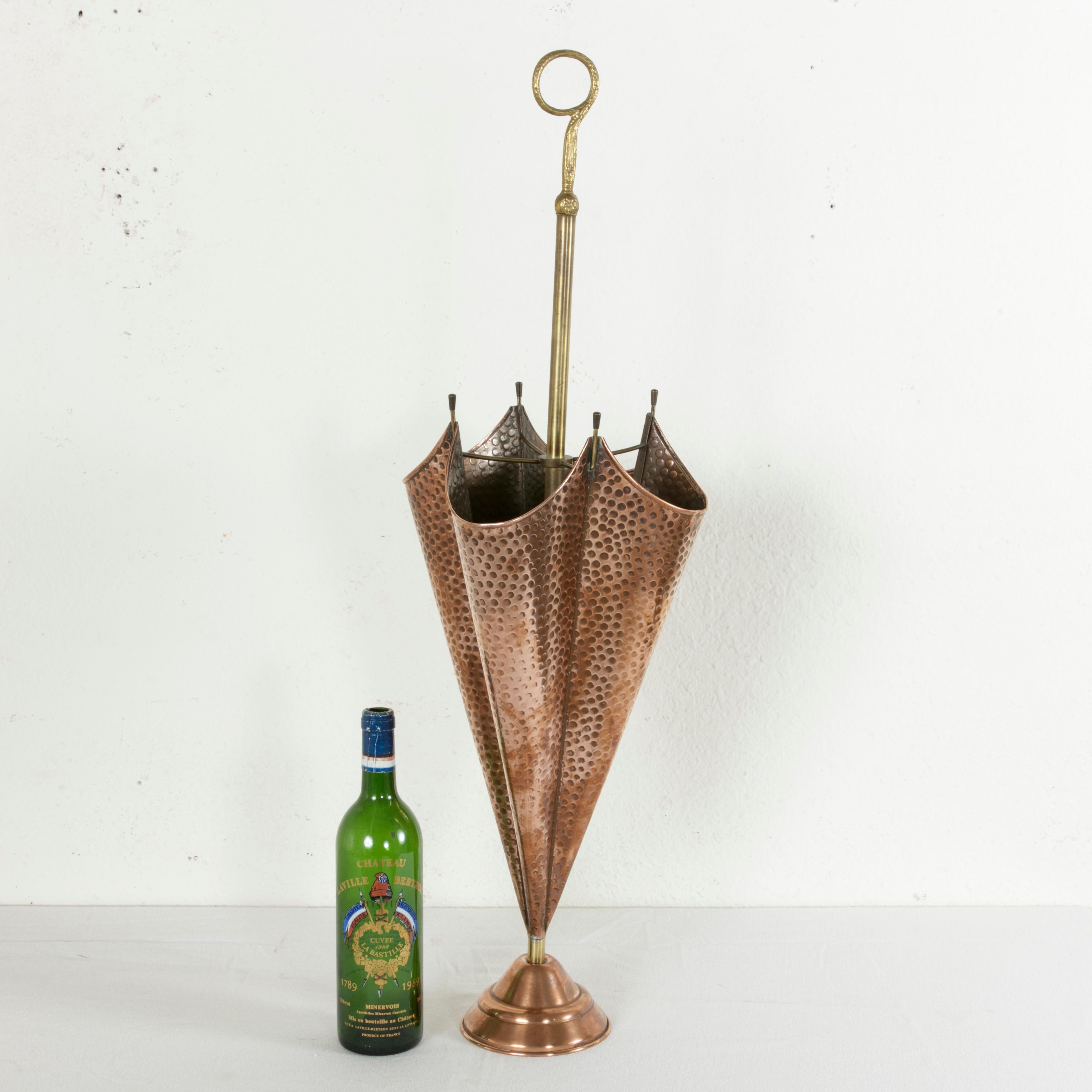 This midcentury copper and brass umbrella stand takes the form of an open umbrella resting on a copper footed base. The umbrella form is dimpled to mimic hand hammering, and the handle is in the form of a spiraled ring. Its narrow diameter and