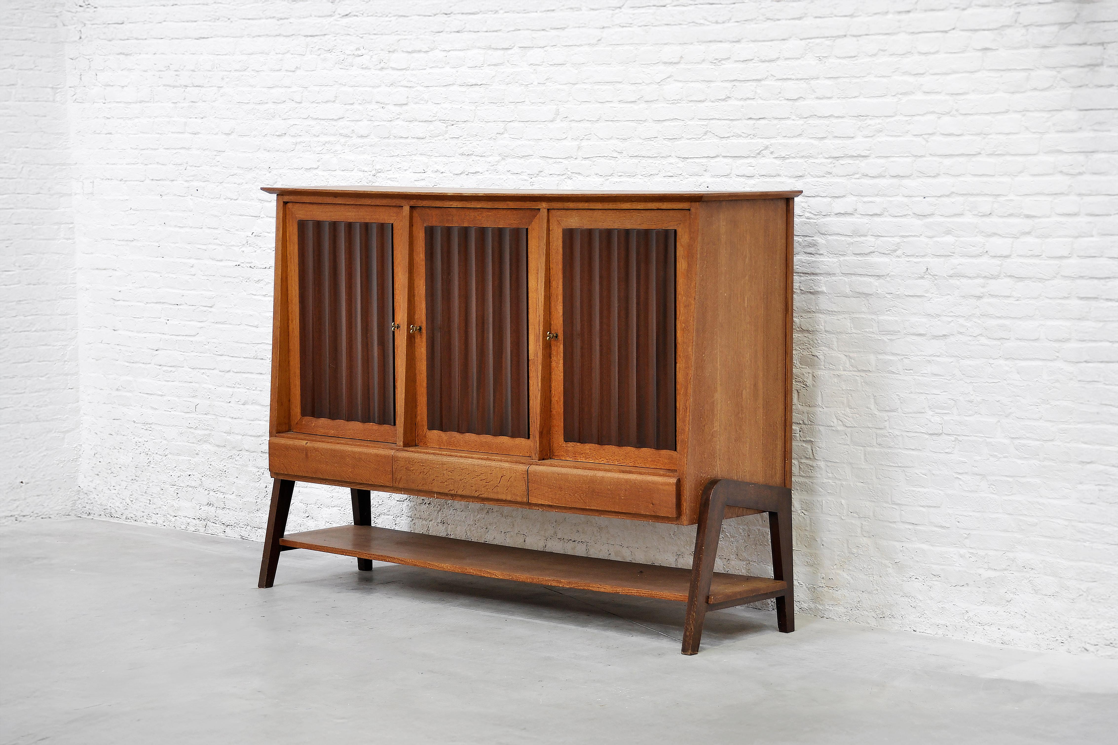 Questa squisita credenza francese degli anni '50 incarna l'eleganza della metà del secolo. Il pezzo presenta quattro ante scanalate in legno riccamente tinto, completate da un piano decorativo in parquet. Poggia su una base angolata con piedi che ne