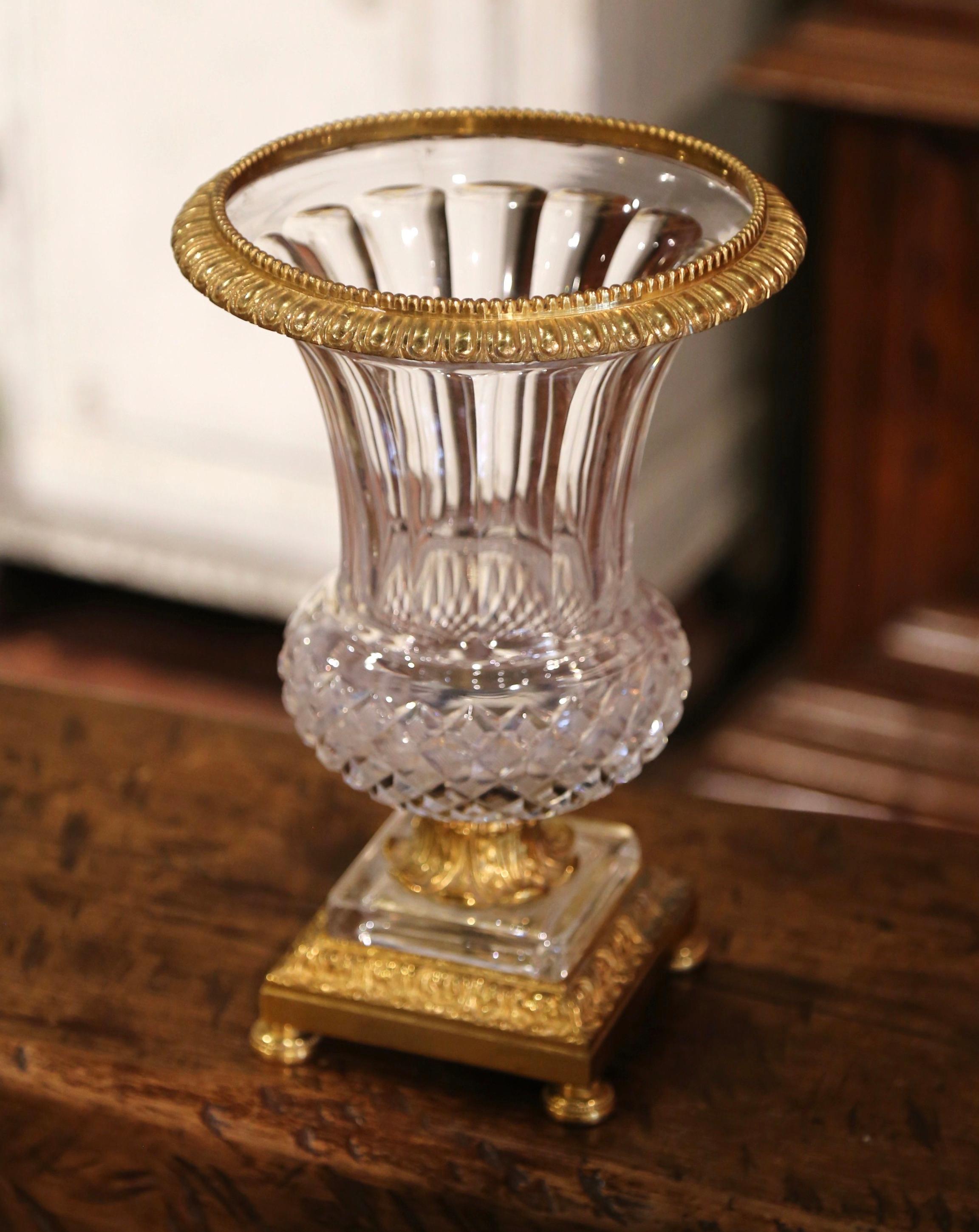 Created in France circa 1960, the elegant antique vessel shaped as a Medici vase is made of cut crystal decorated with bronze dore mounts; the vase stands on a square bronze base decorated with geometric motifs and ending with bun feet. The top is
