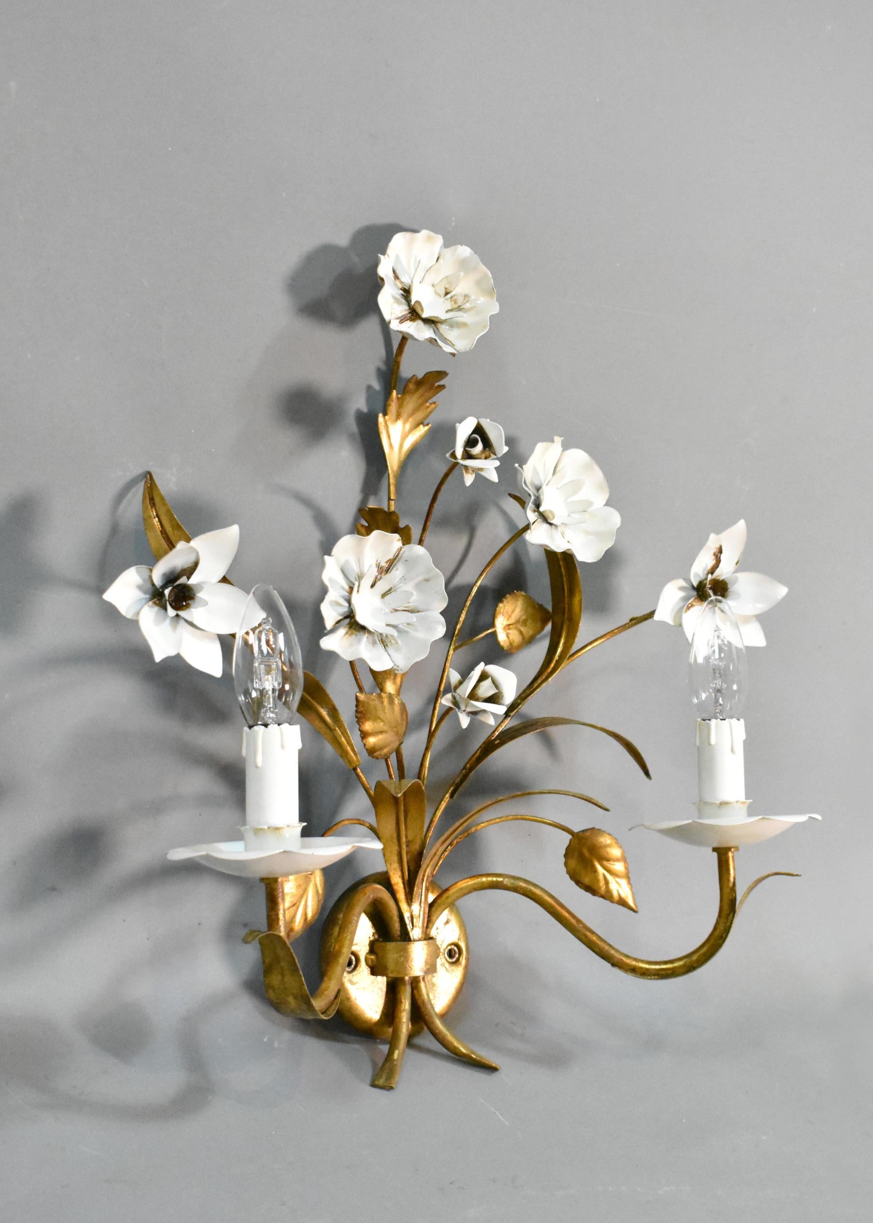 A pretty Hollywood Regency mid-century toleware wall light / sconce featuring a variety of white flowers and gilded foliage.

This two-light wall sconce has elegant stems and flowers extending out from the central base.

This light has been tested