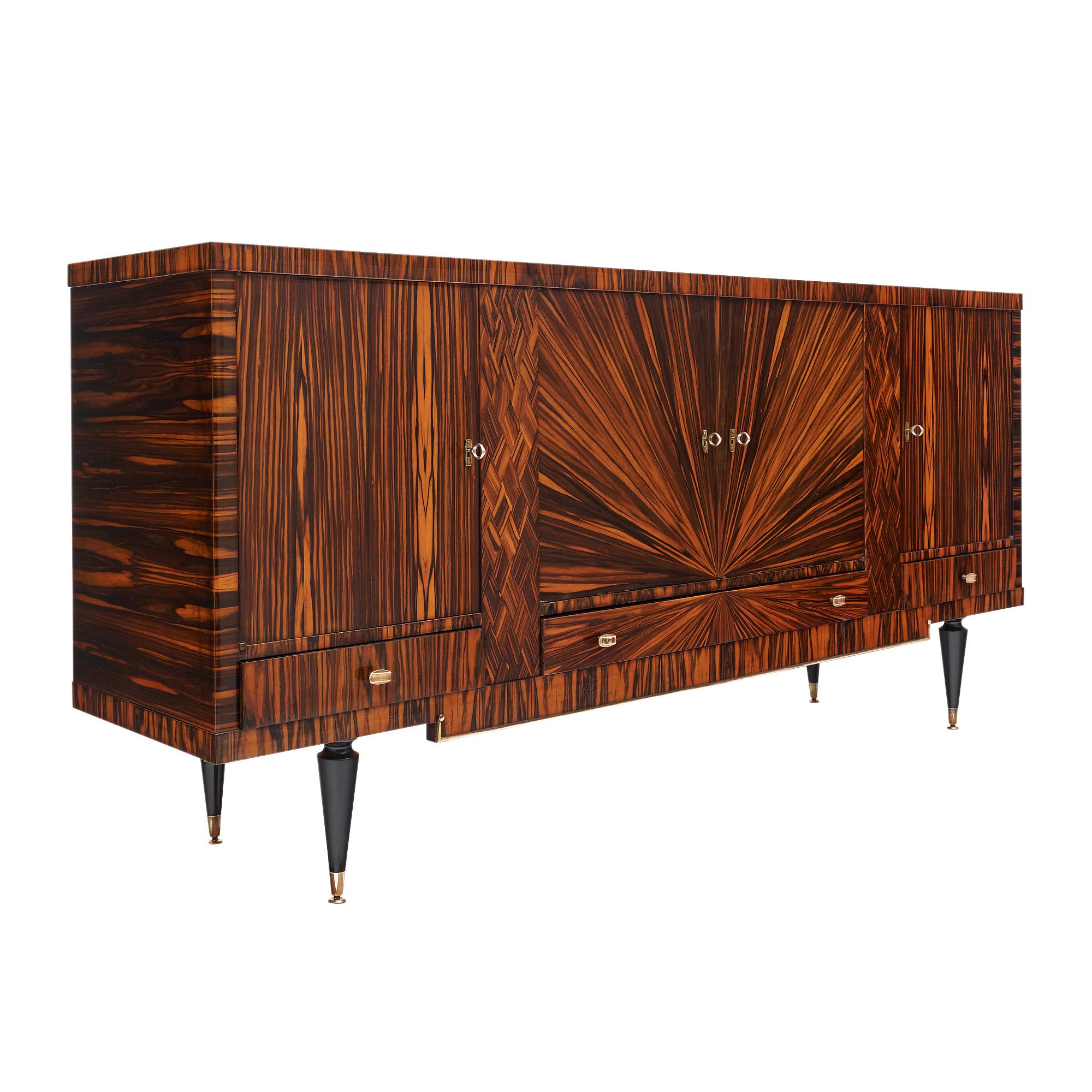 Buffet/Enfilade del periodo modernista francese. La credenza vanta una spettacolare impiallacciatura con motivo a sole sulla facciata e un intarsio cubico. Quattro porte si aprono su interni in legno satinato con scaffali in legno. Inoltre, il