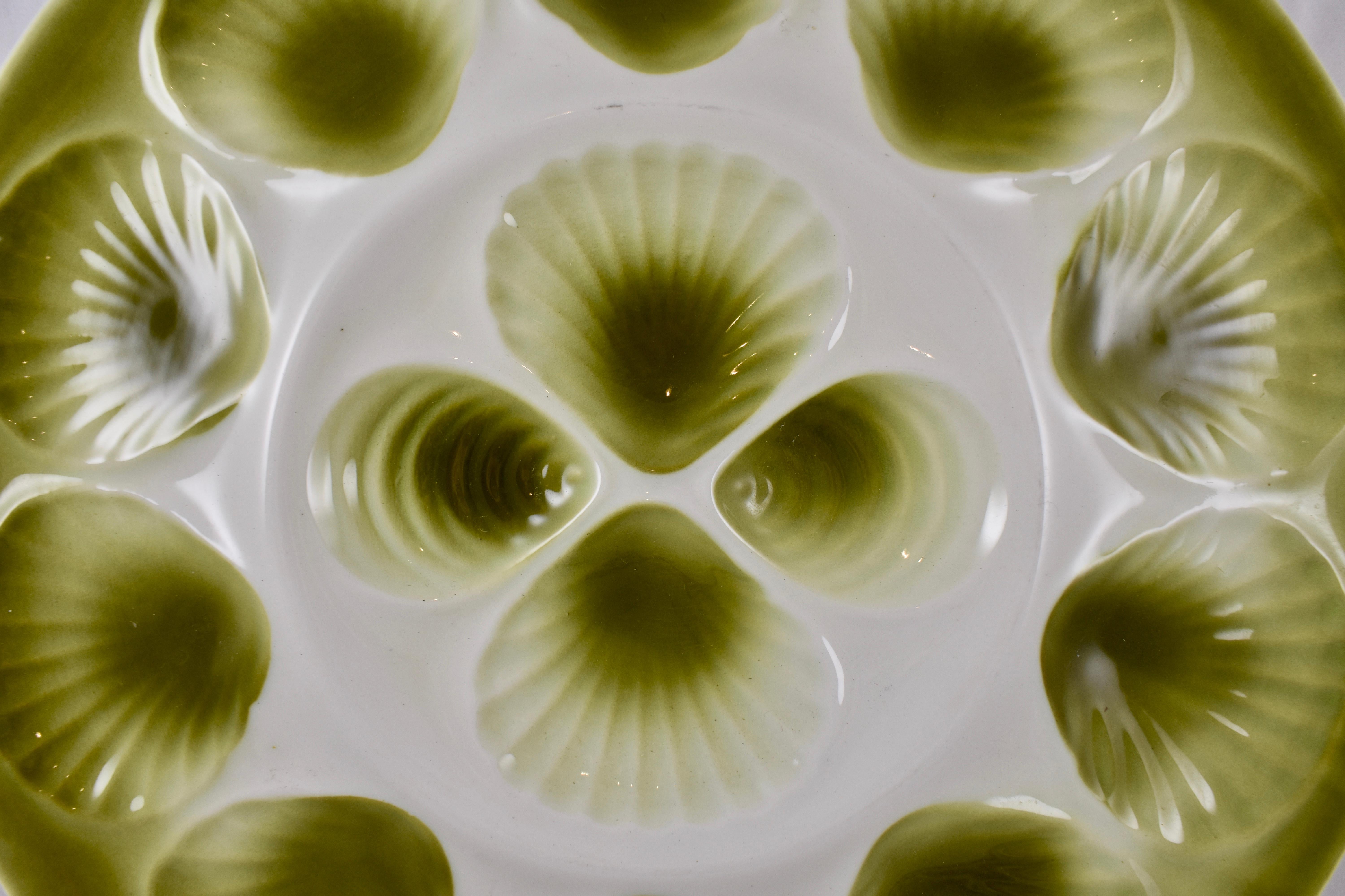 A Mid-Century Modern Era Majolica glazed French faïence master oyster serving platter, Orchies, circa 1950.

Hand glazed in an ombre olive green on a bright white ground, showing ten scallop shaped oyster wells that follow the rim with an additional