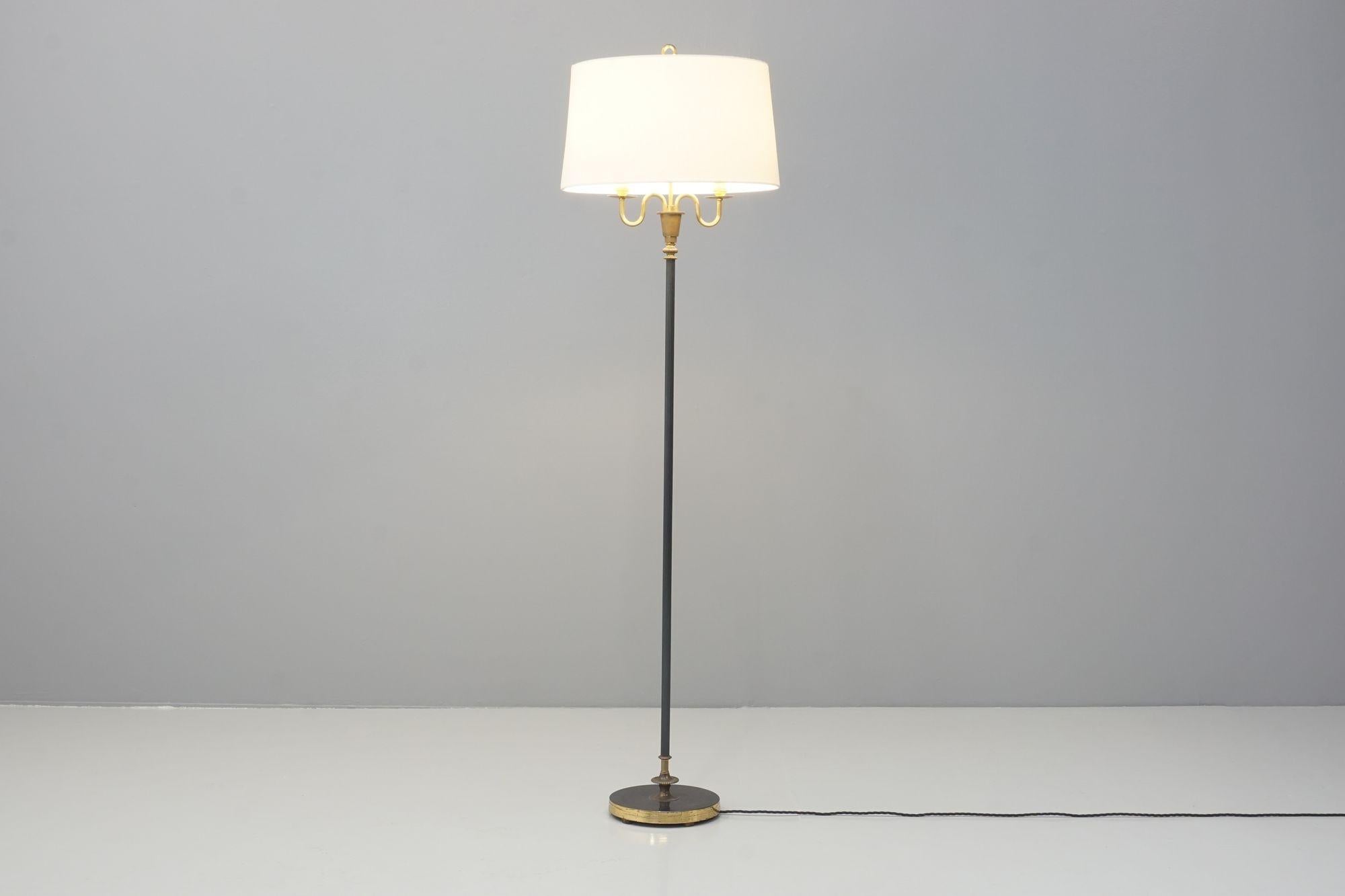 A Mid-Century French floor lamp with a blackened steel shaft and base, with brass details at the base and neck. Double stem neck with the original shade that has been newly covered in cream fabric. The lamp has been re-wired and tested.