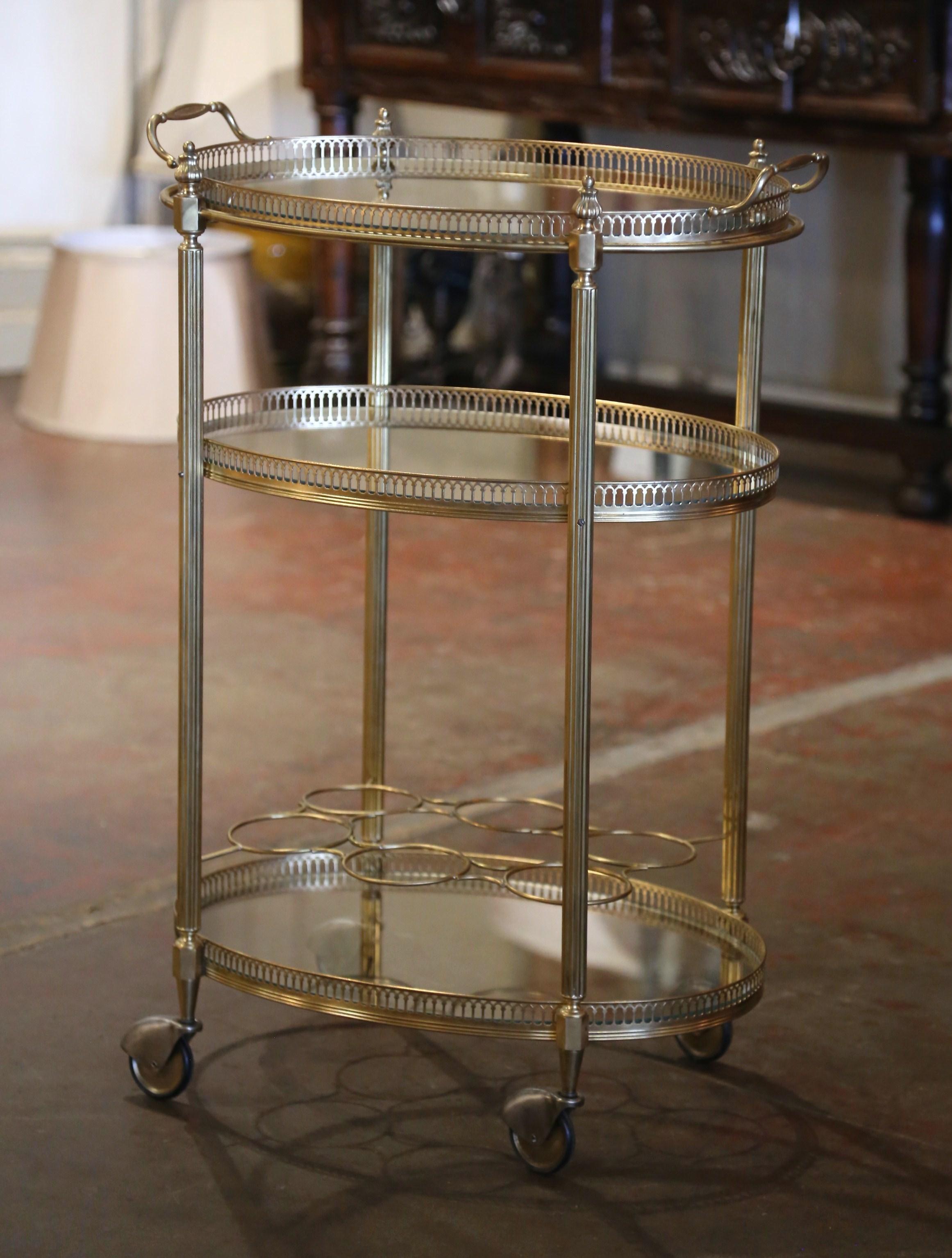 This elegant vintage rolling bar cart was created in France, circa 1960. Built in brass and oval in shape, the three-tier plateau trolley stands fluted legs supports topped with decorative finials, and ending with casters at the base. The top deck,