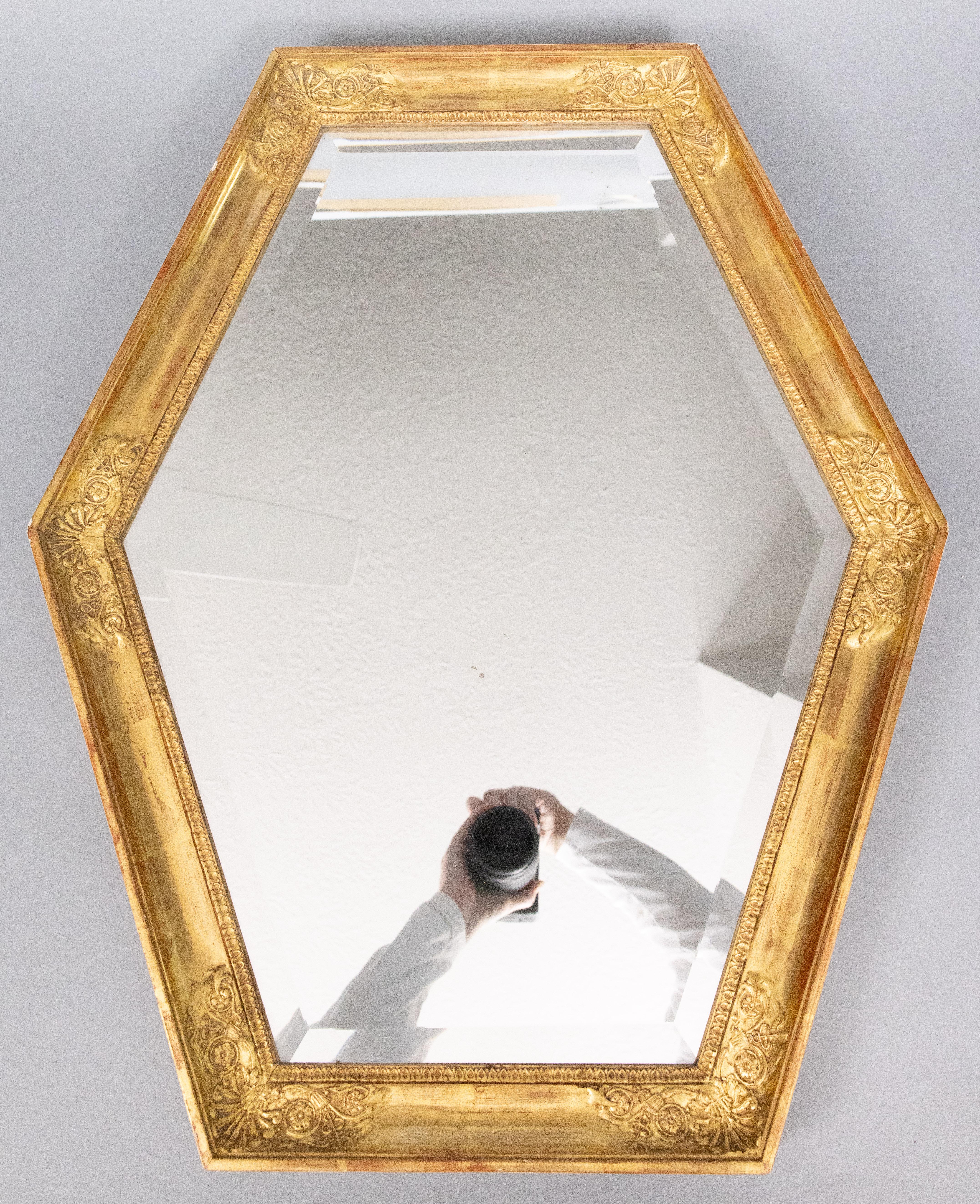 Impresionante espejo francés vintage de madera dorada, con el cristal biselado original y soporte de madera, hacia 1950. Este fino espejo tiene una elegante forma hexagonal y preciosos detalles florales en una hermosa pátina dorada. Tiene un buen