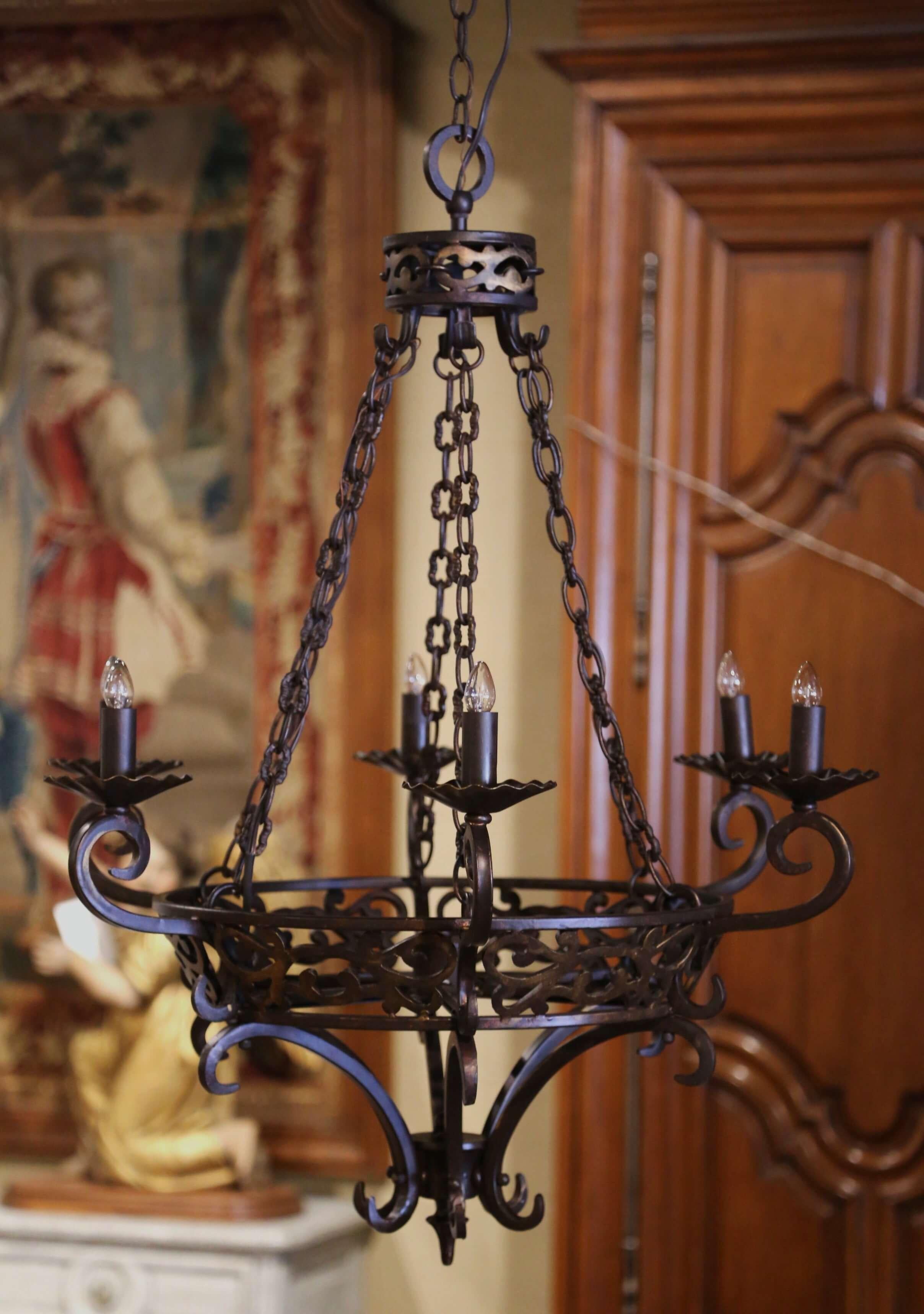 This intricate antique iron light fixture was forged in France circa 1960. Round in shape, the Gothic chandelier features scrolled decor under the large circle. The fixture is secured with four chains connected to a decorative canape at the top. The