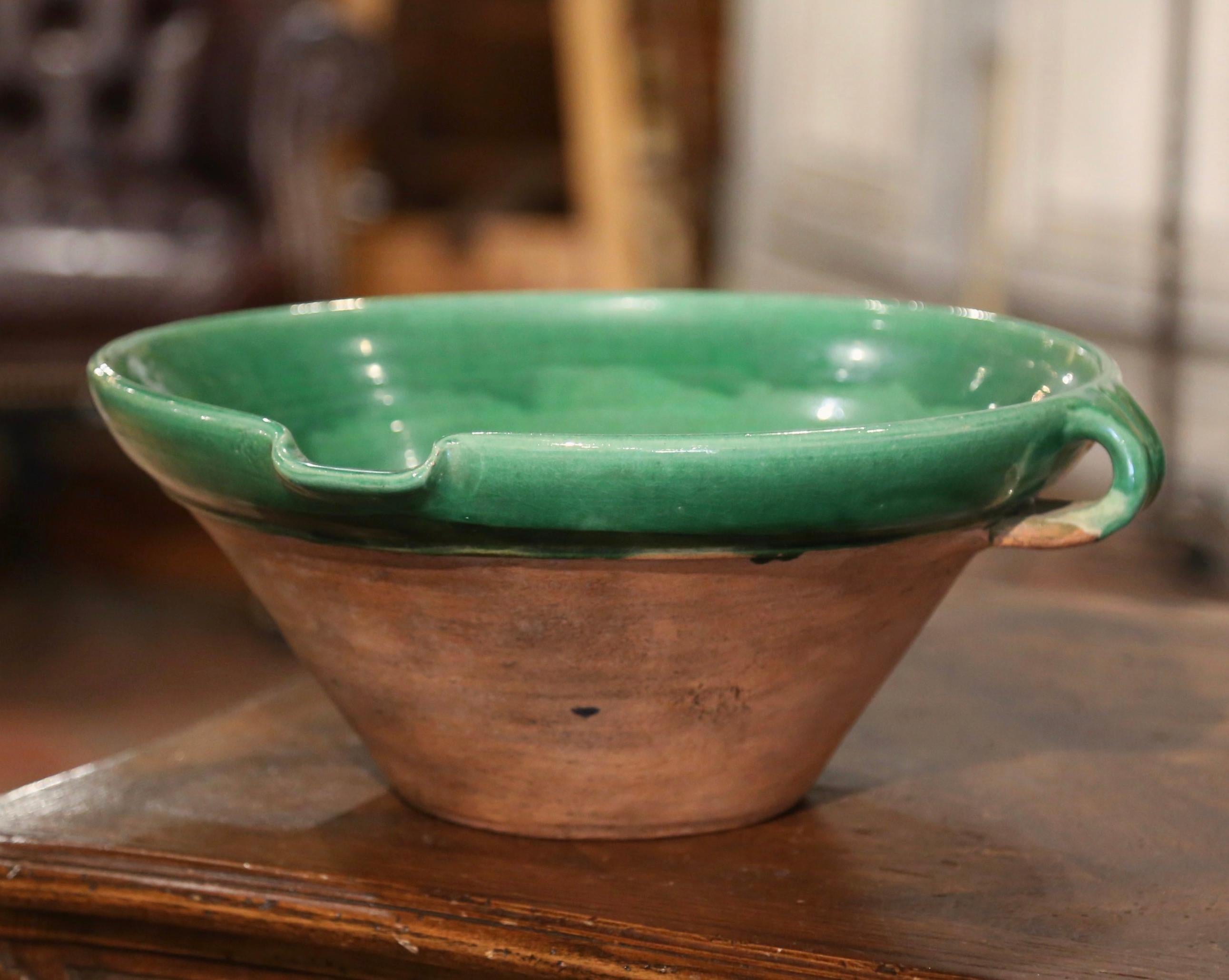 Diese elegante antike Tian (provenzalische Bezeichnung für Schale) wurde um 1970 in der Provence, Frankreich, hergestellt; die runde, handgefertigte Terrakottaschale hat zwei kleine Henkel, einen Dienerschnabel und eine dezente grüne Glasur auf der