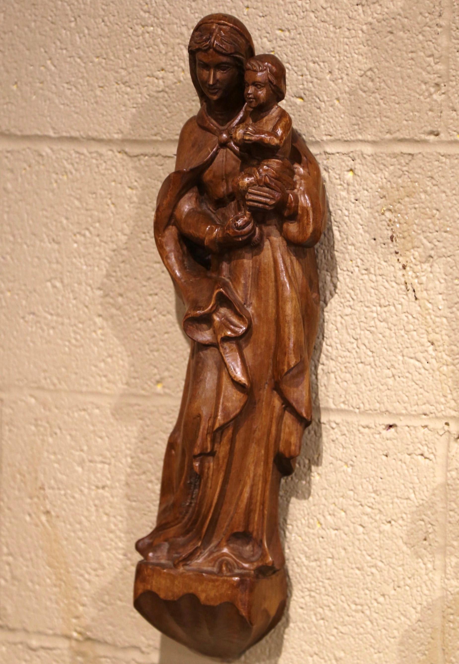 Diese elegante antike Wandstatue der Mutter mit Kind wurde um 1960 in Südfrankreich geschnitzt. Die große, verführerische Skulptur in Hochrelief zeigt die Madonna, die auf einem aufgesetzten Sockel steht und ihren Sohn, unseren Herrn Jesus Christus,
