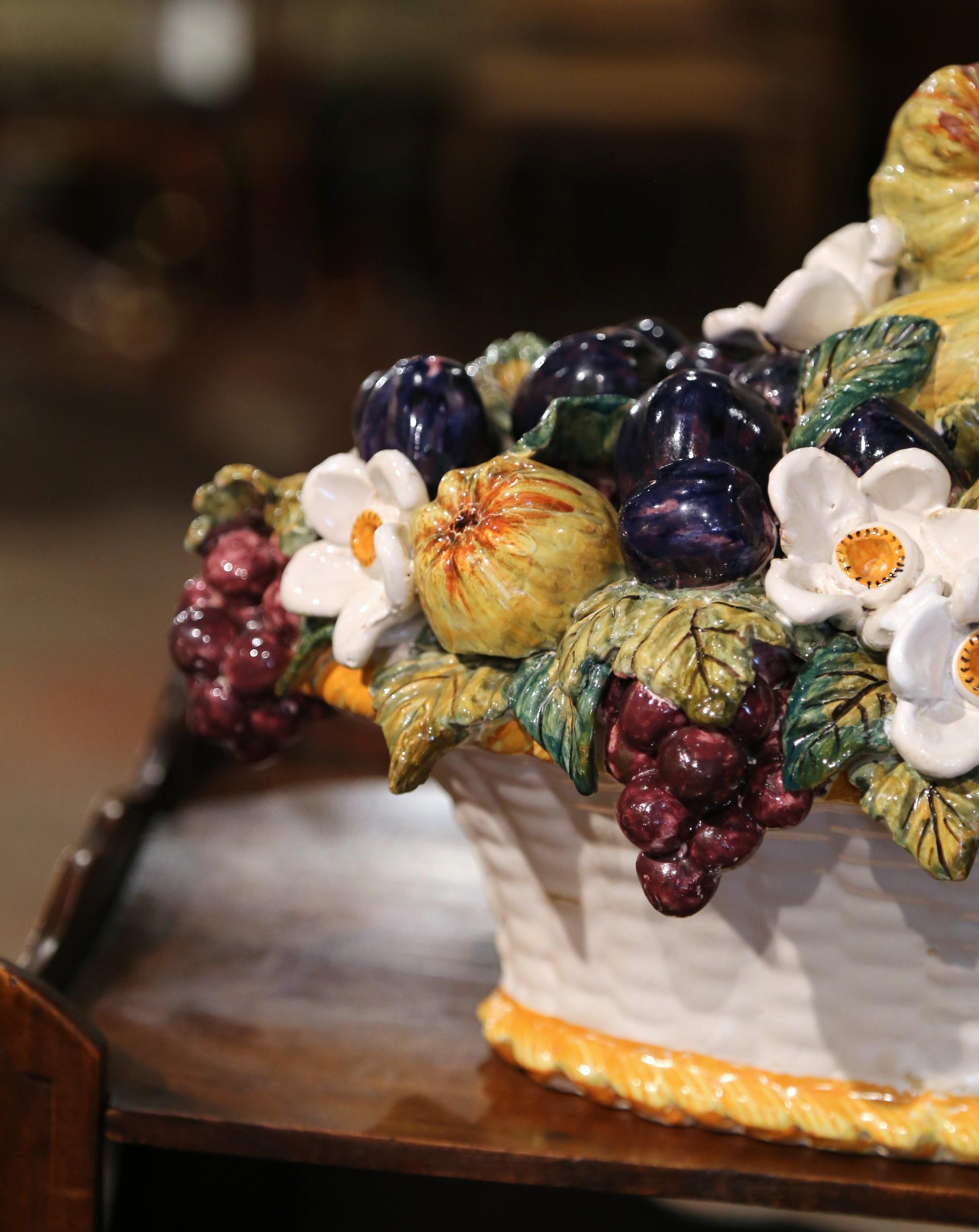 Decorate a tabletop with this colorful, majolica basket composition. Crafted in France circa 1960, the centerpiece features a realistic assortment of fruits and vegetables in high relief set inside a white basket decorated with a weave motif. The