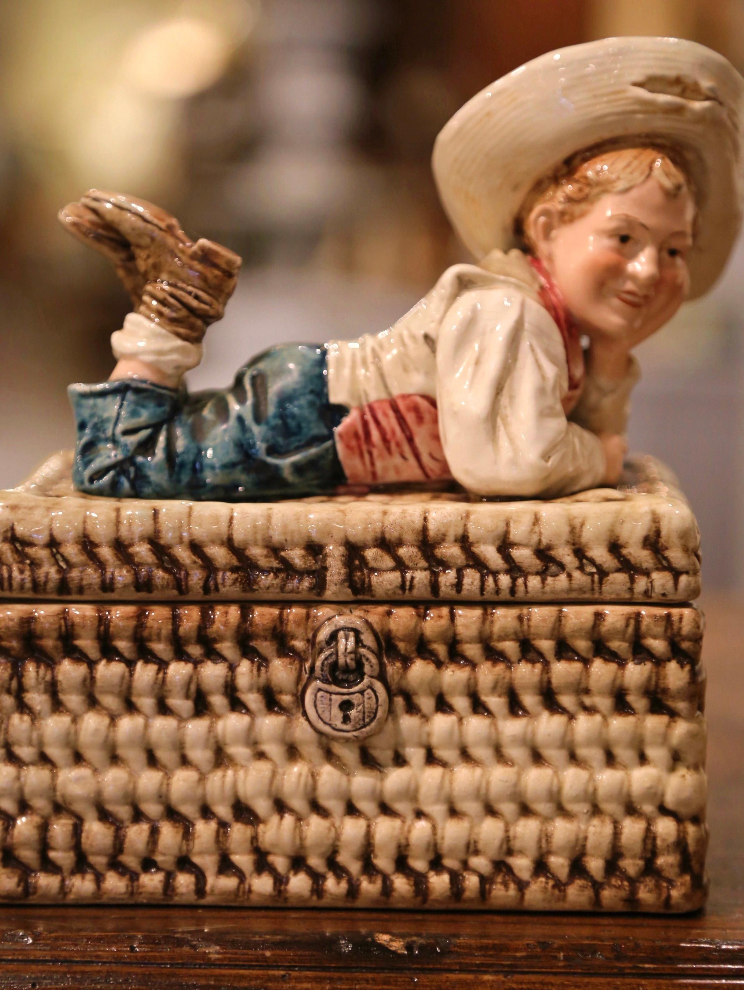 Decorate a shelf with this elegant antique Majolica box. Crafted in France circa 1950, the decorative and whimsical casket is decorated on all four sides in realistic high relief weave motifs. The removable lid features a bohemian figure lying on