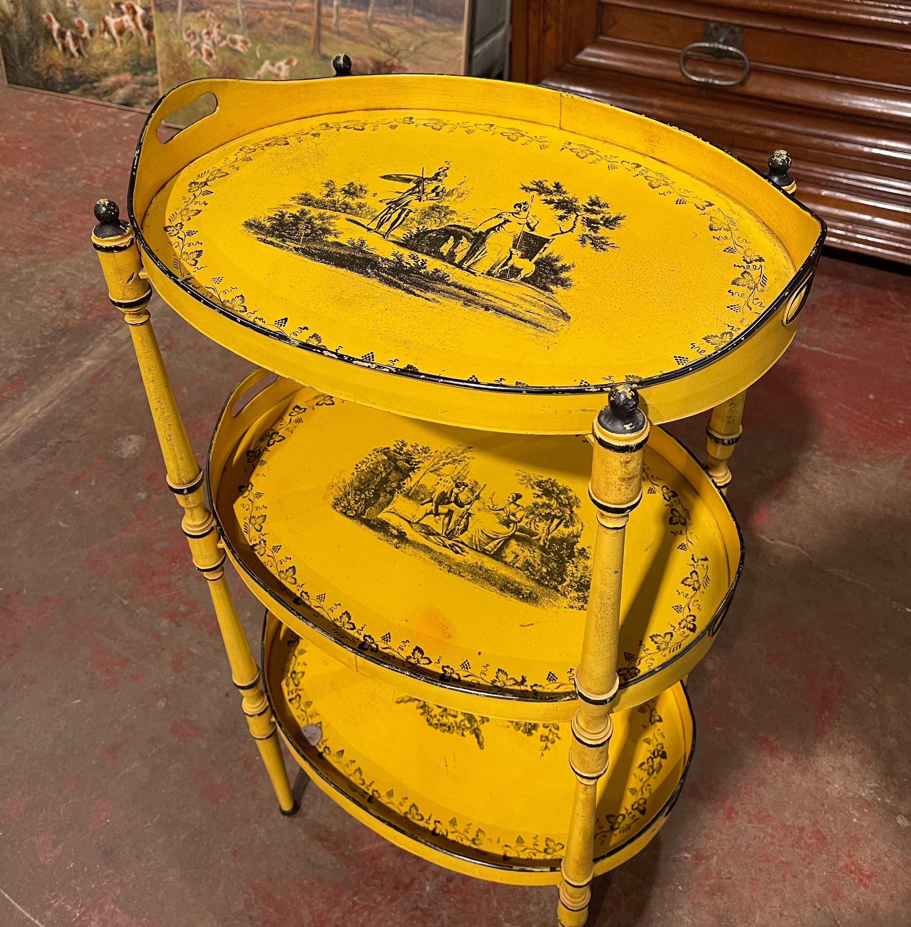This colorful table was crafted in France circa 1960. Made of metal, the occasional table stands on rounded tapered legs and features three removable trays dressed with side handles; each plateau is hand painted with courting scenes and floral