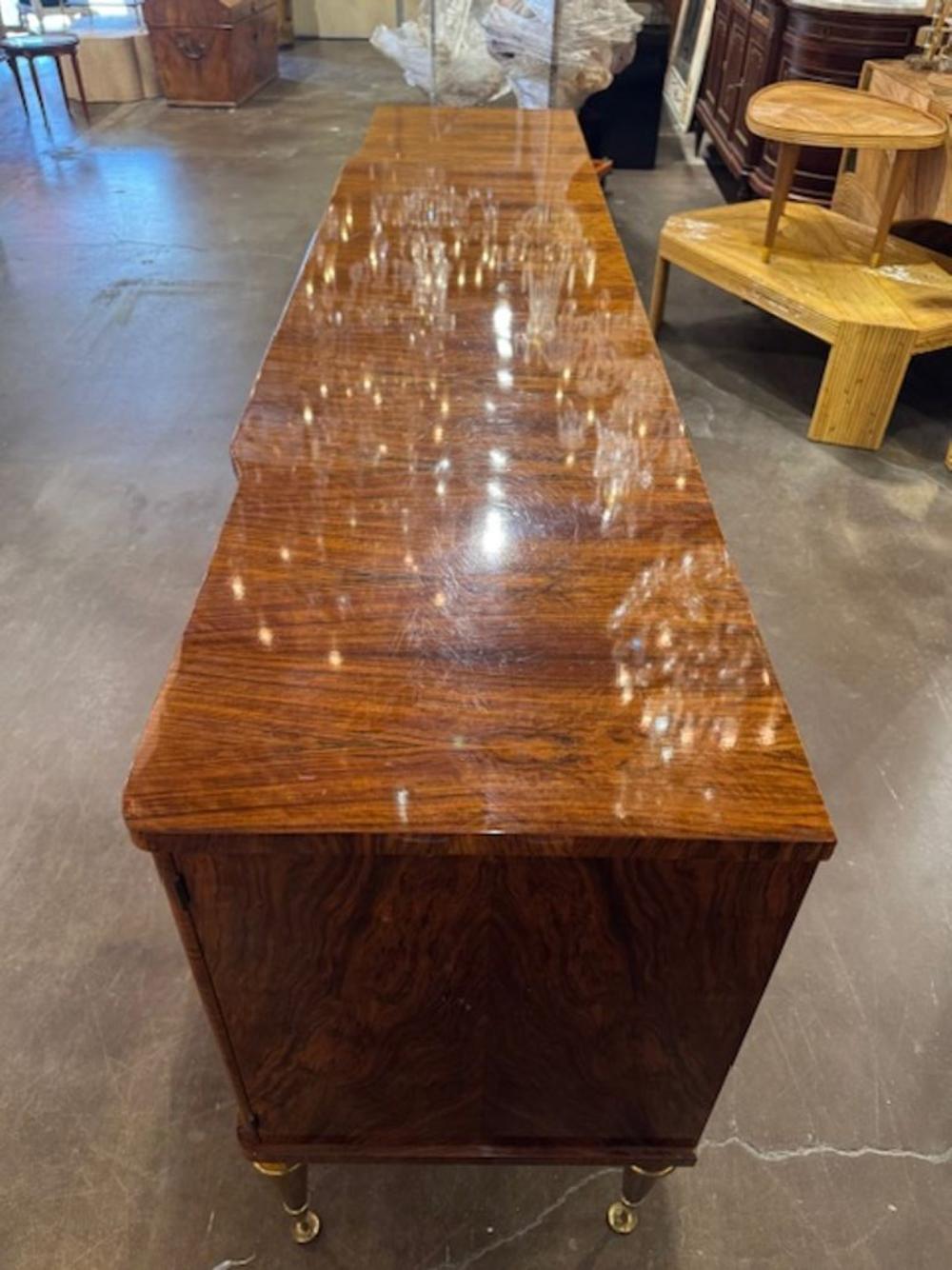 This Mid Century French Inlaid Sideboard with Brass Details is a stylish and elegant piece of furniture that embodies the Mid-Century Modern aesthetic. This piece features intricate inlay and brass details that add a touch of sophistication to any