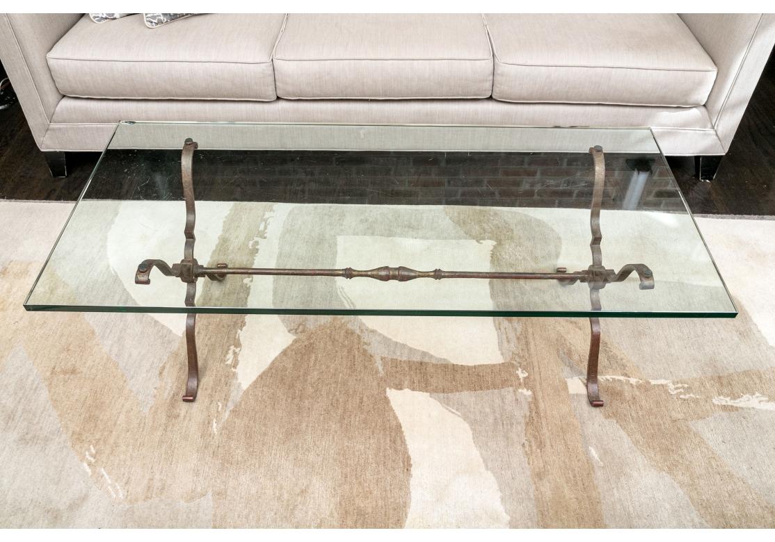 Une table à cocktail française raffinée avec une base en fer à volutes patinée dans une finition dorée profonde avec une taille rouge apparaissant à travers et ayant un plateau en verre entièrement biseauté de 3/4