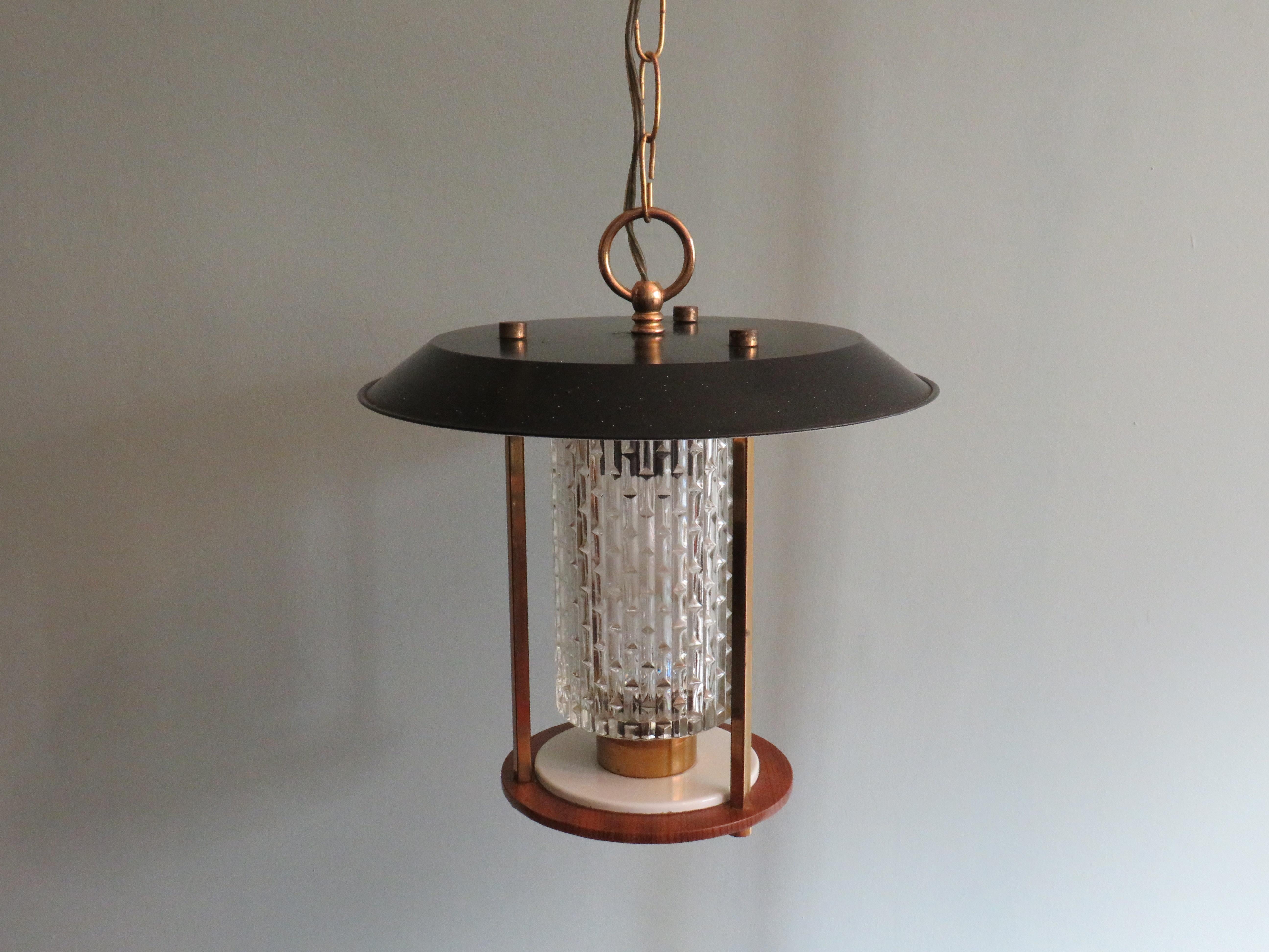 This round French lantern consists of a teak wooden plateau, a glass chalice with a graphic motif and a black metal cover plate.
The frame and suspension are made of brass.
The lamp is provided with 1 E 27 fitting and a complete suspension