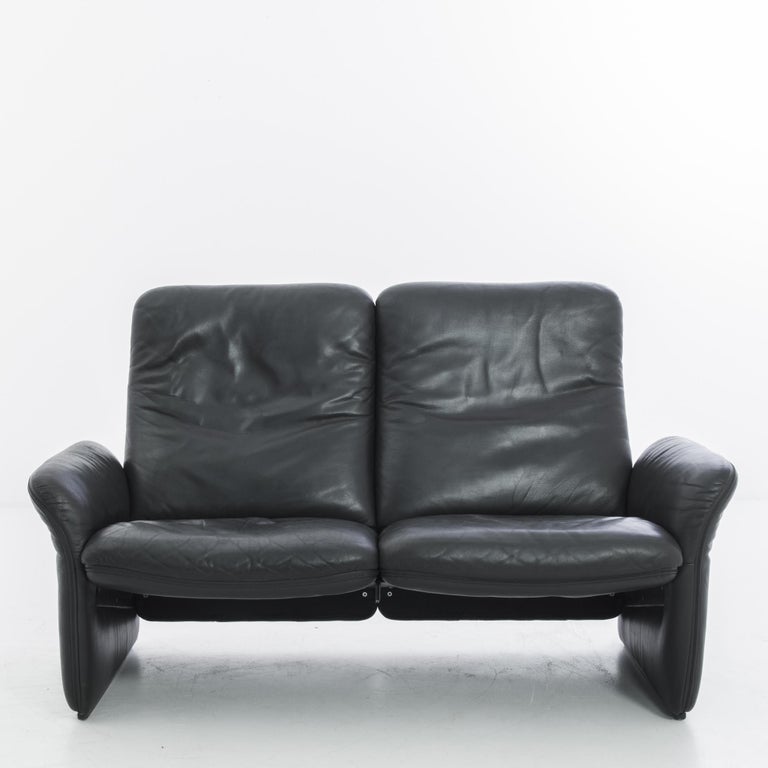 A leather sofa from 1950s France. A dynamic Modernist take on the loveseat: streamlined black leather creates a comfortable seat for two. The curve of the armrests provides structural support, producing the illusion of a floating seat. The generous