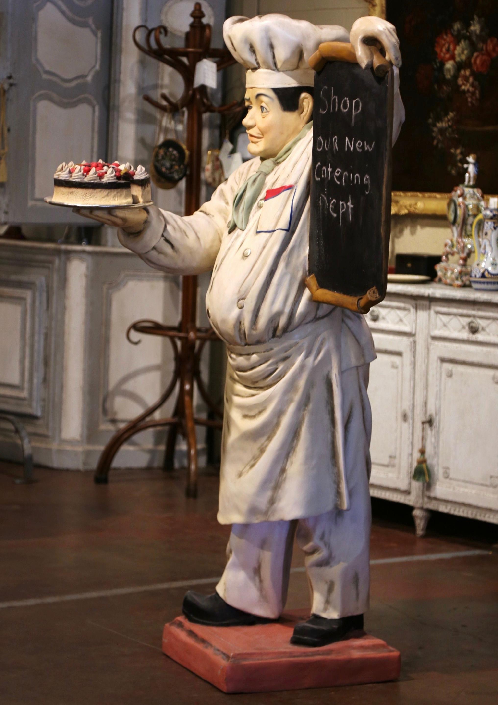 Decorate a restaurant or a bakery with this antique display chef sculpture. Crafted circa 1960, the vintage statue composition features a life size cheerful baker chef holding a cake in one hand, while holding a chalk menu board in the other. The