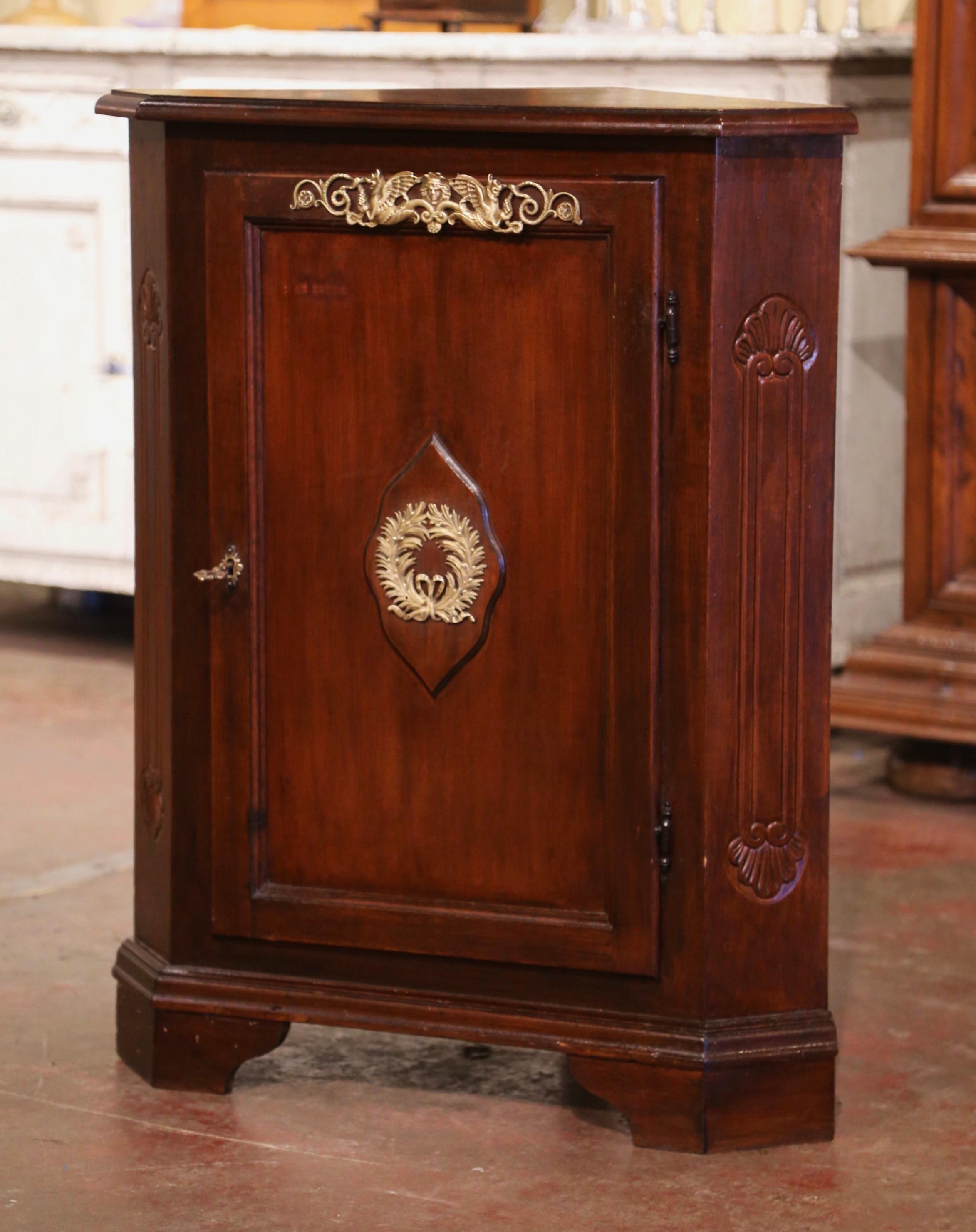 This elegant antique corner cabinet was created in France circa 1950. Built of mahogany wood, the cupboard stands on bracket feet over a straight plinth. The small buffet is fitted with a single door with recessed panel and embellished with a brass