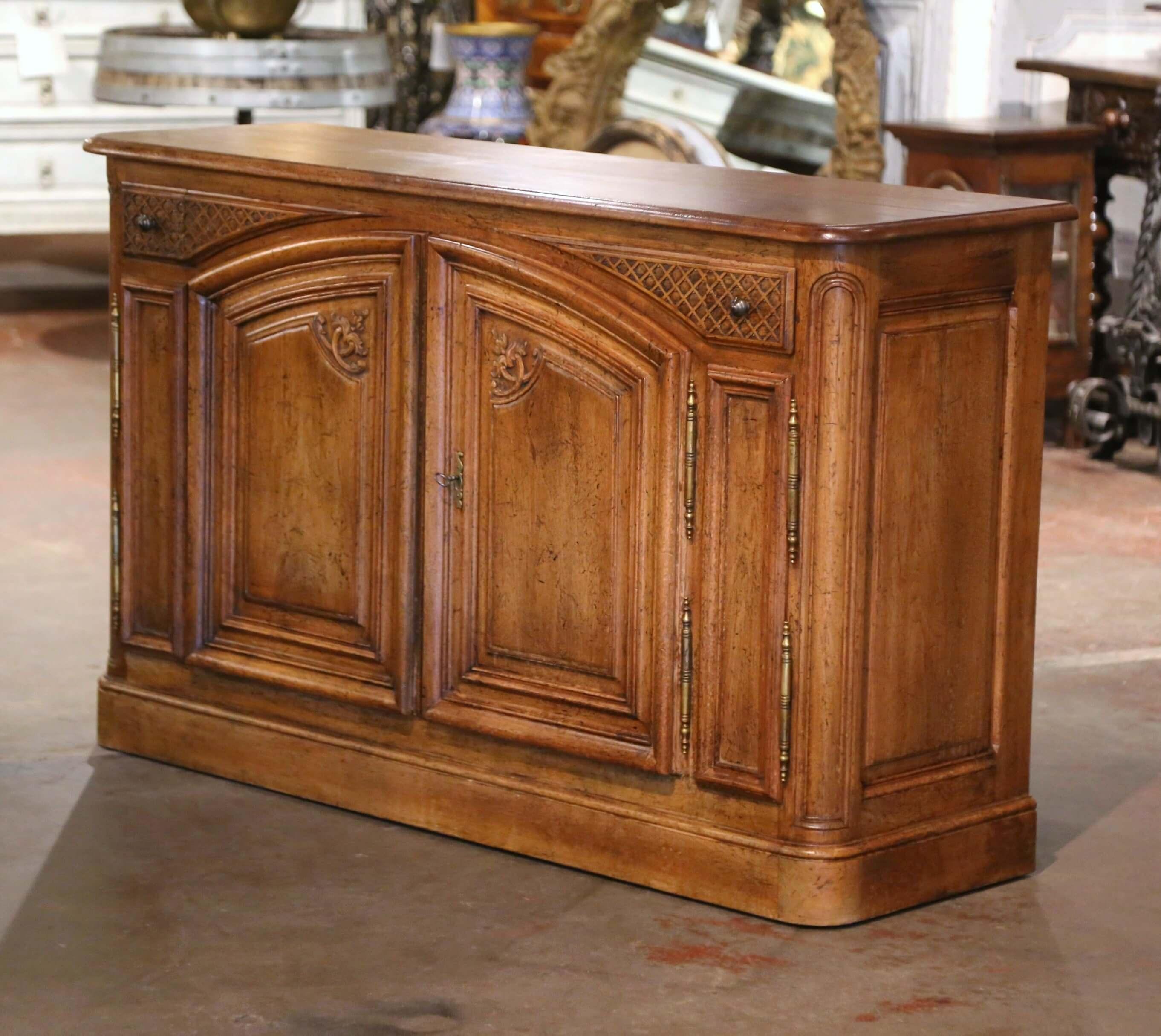 Decorate an entry or a living room with this elegant buffet. Crafted in France circa 1970, and built of walnut, the cabinet stands on a thick plinth base. The piece features two arched paneled doors decorated with carved floral motifs in the