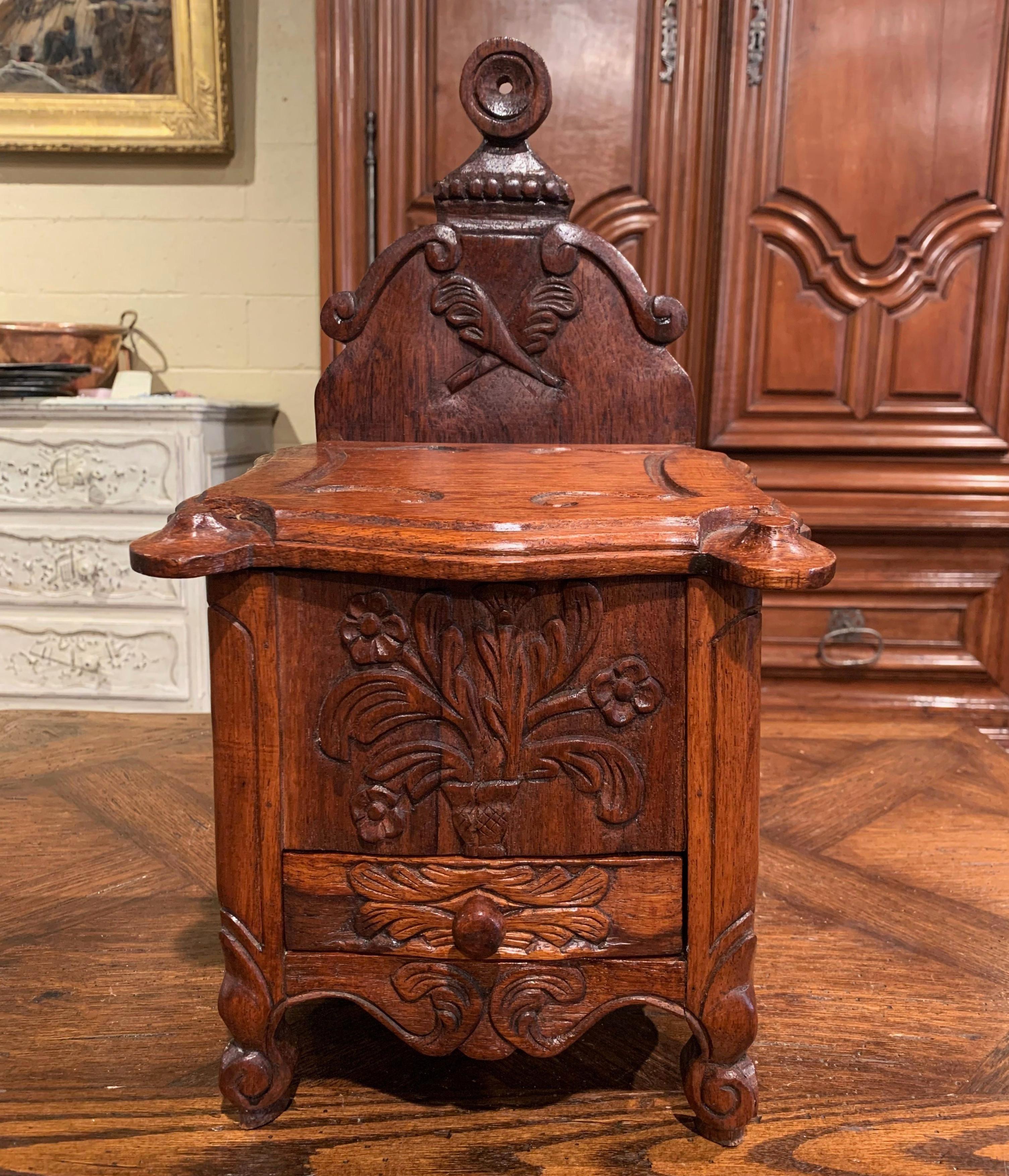 This elegant, antique salt box was crafted in southern, France, circa 1950. The ornate decorative box sits on delicate escargot feet over a scalloped apron; it is decorated with beautiful carvings throughout including floral and torch motifs. The