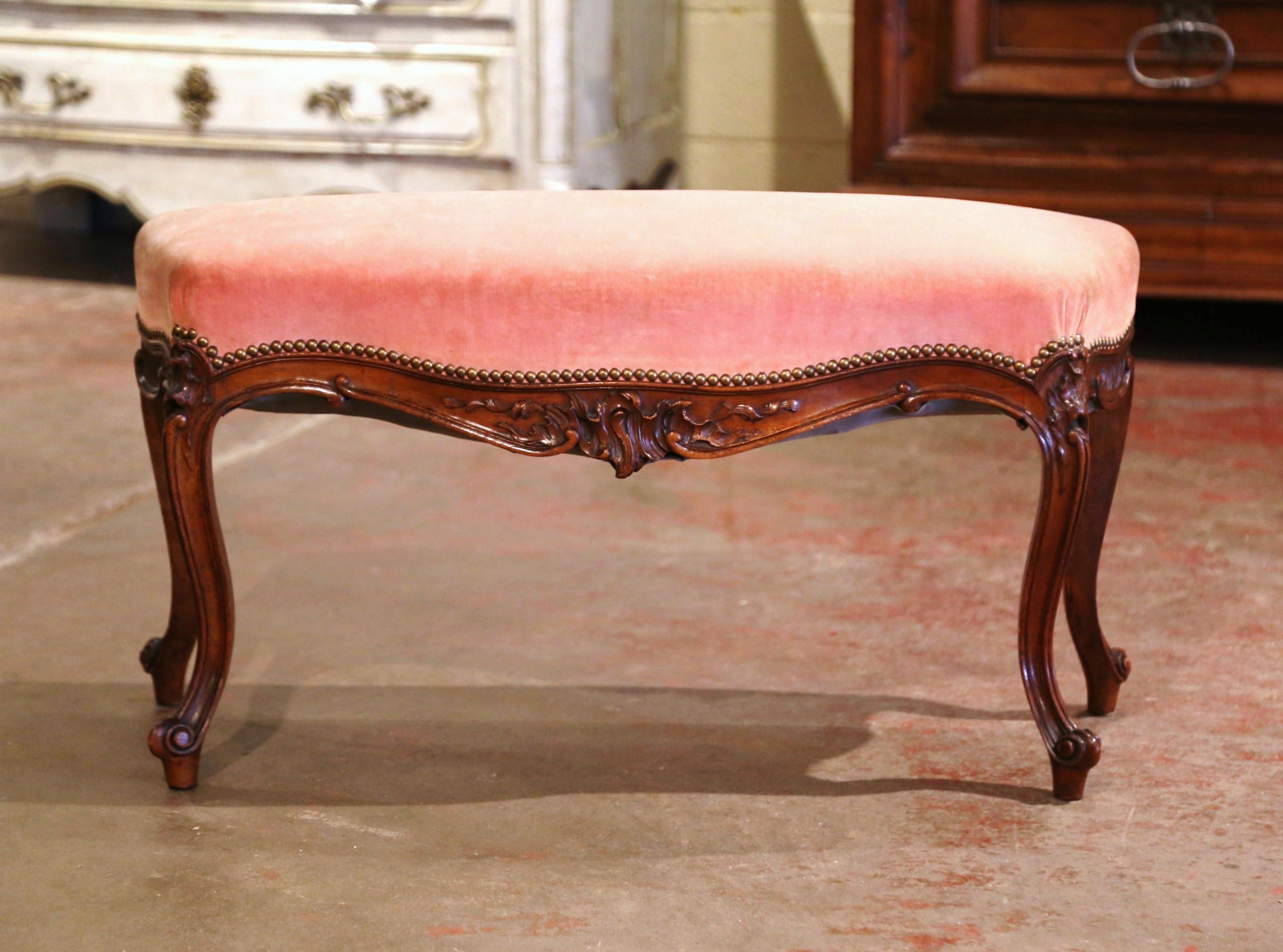 Crafted in Provence, France circa 1960, the antique fruitwood piano bench stands on cabriole legs decorated with floral motifs at the shoulder, and ending with escargot feet. The bombe scalloped apron and curved sides are decorated with hand carved