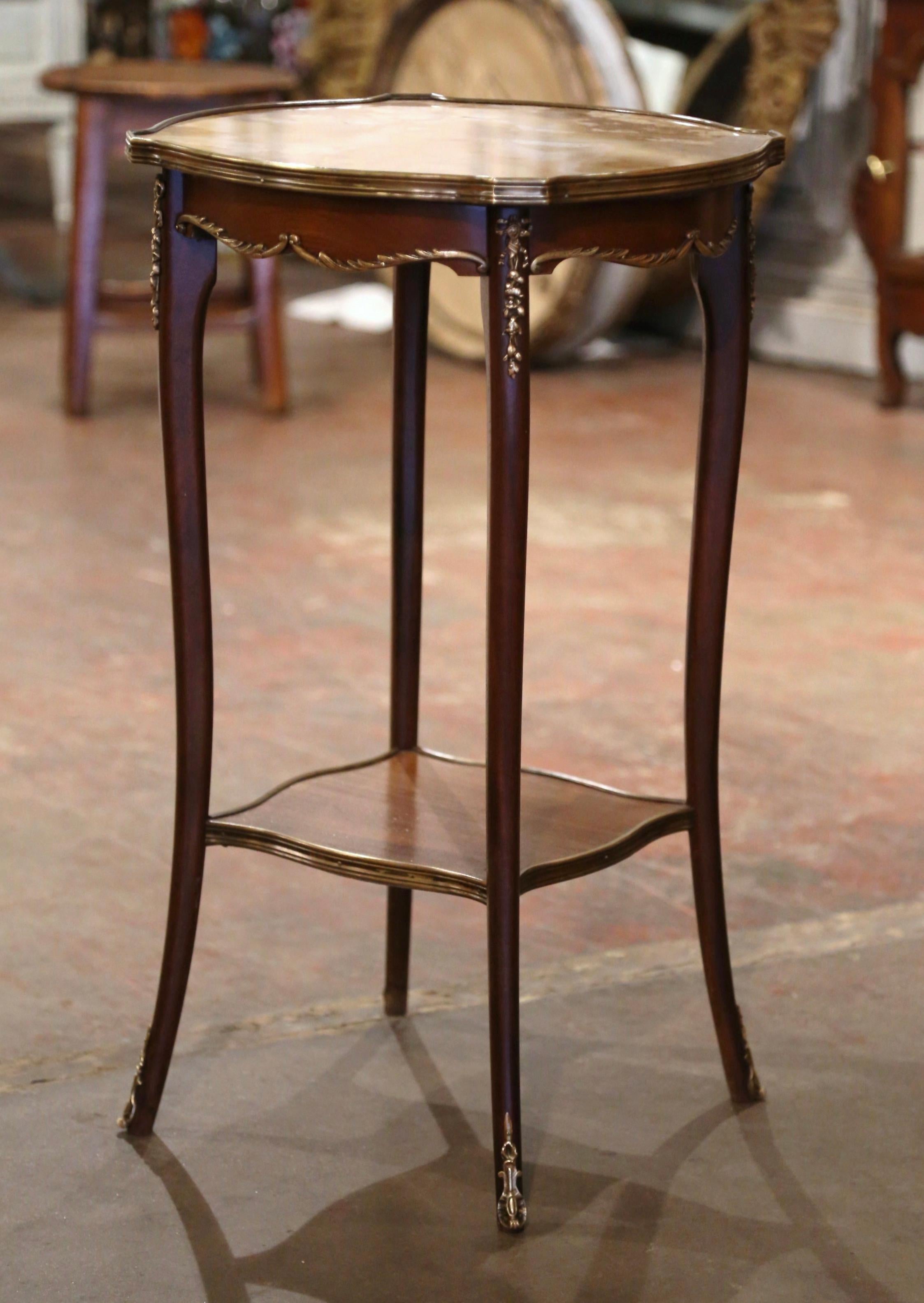  Decorate a den with this elegant antique side table. Crafted in France circa 1950, and round in shape with recessed corners, the table sits on cabriole legs dressed with decorative bronze mounts at the shoulders and ending with bronze sabots. The