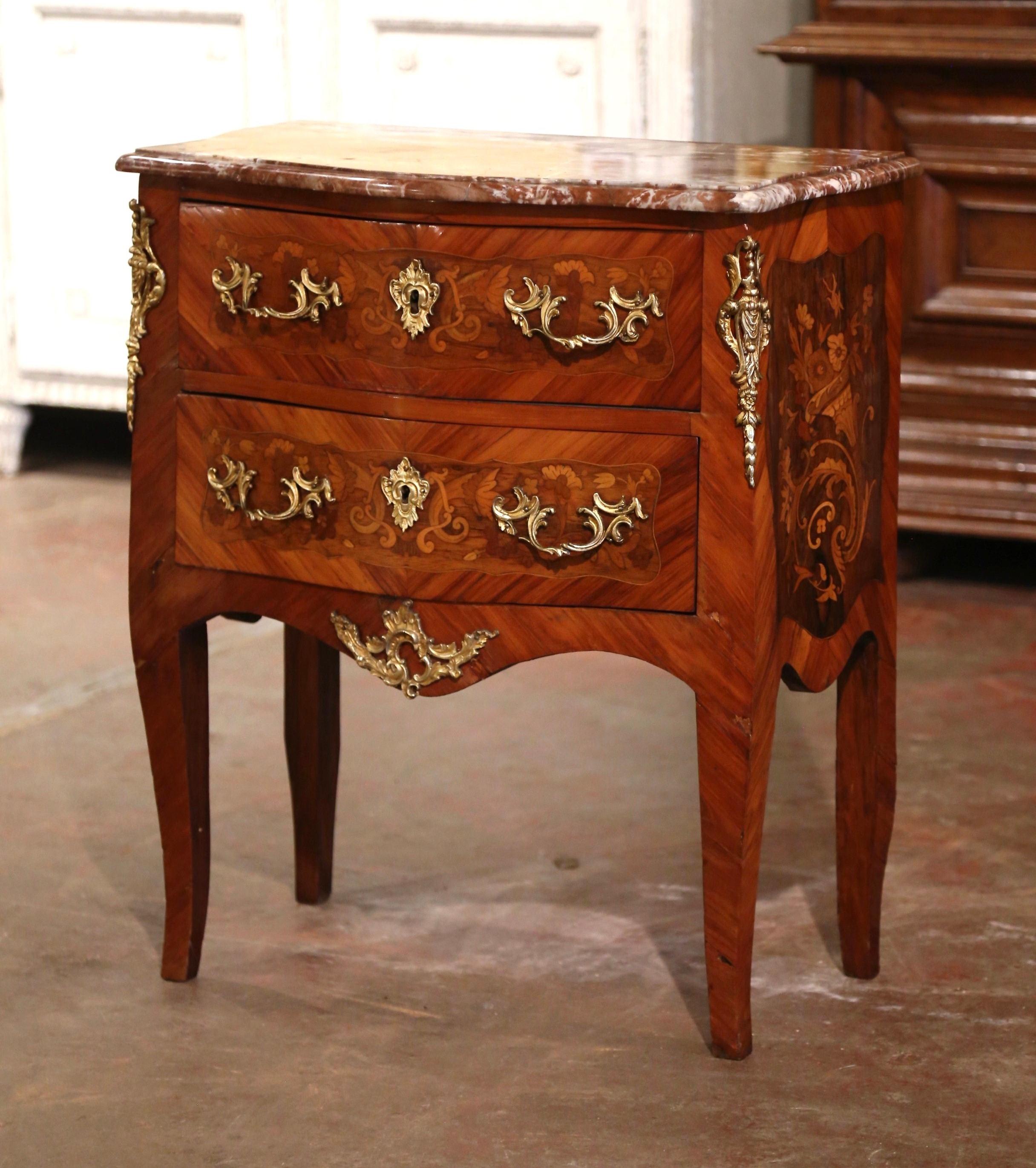 Crafted in France circa 1980, the vintage commode stands on cabriole legs, over a scalloped apron decorated with a center bronze shell and leaf motif mount. The petite fruit wood chest features two bombe drawers across the front embellished with