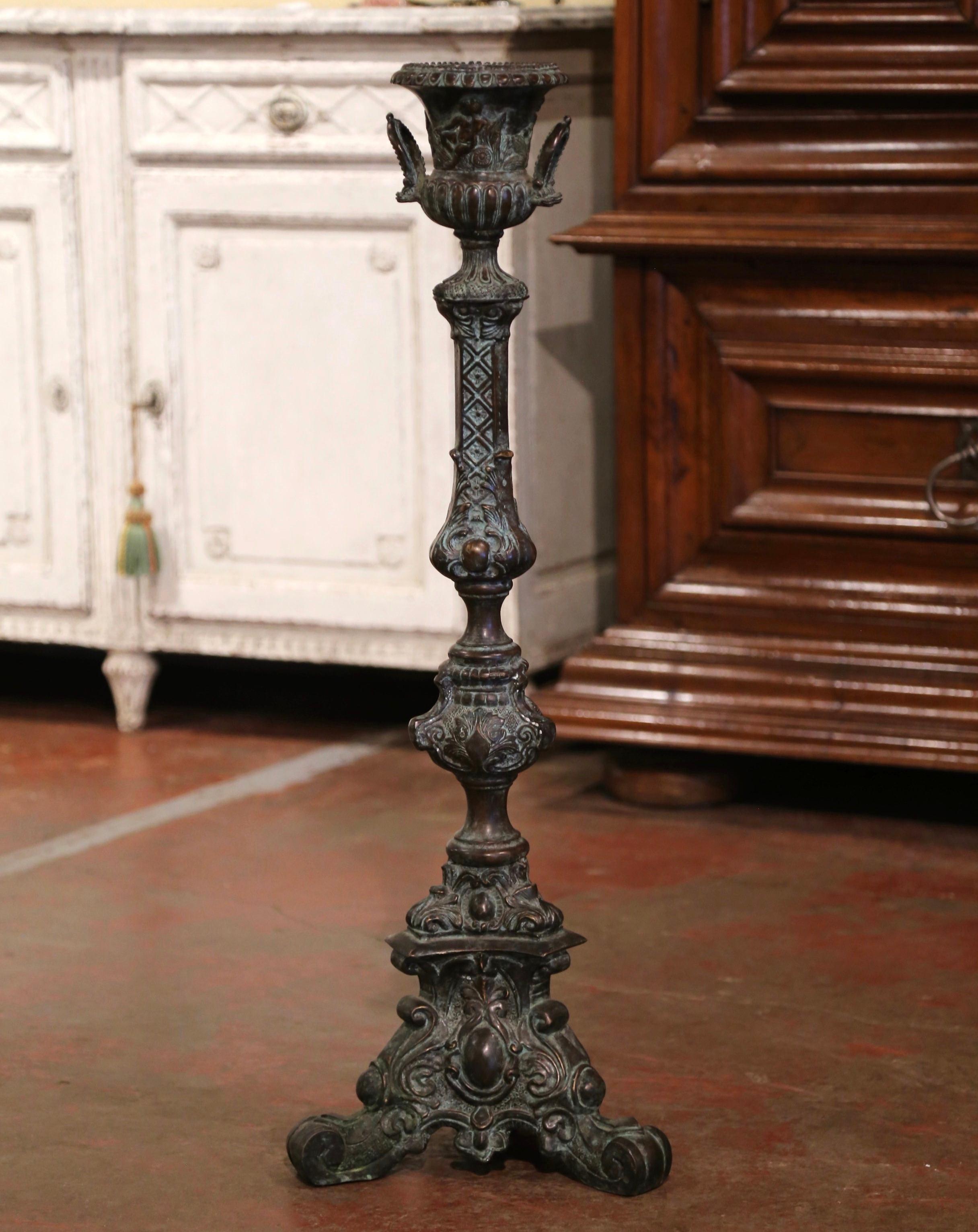 Crafted in France circa 1950 and made of solid bronze, the vintage candle holder stands on a triangular base ending with scrolled feet. The stem is decorated with intricate motifs including Fleur-de-Lis and acanthus leaves. The top is dressed with