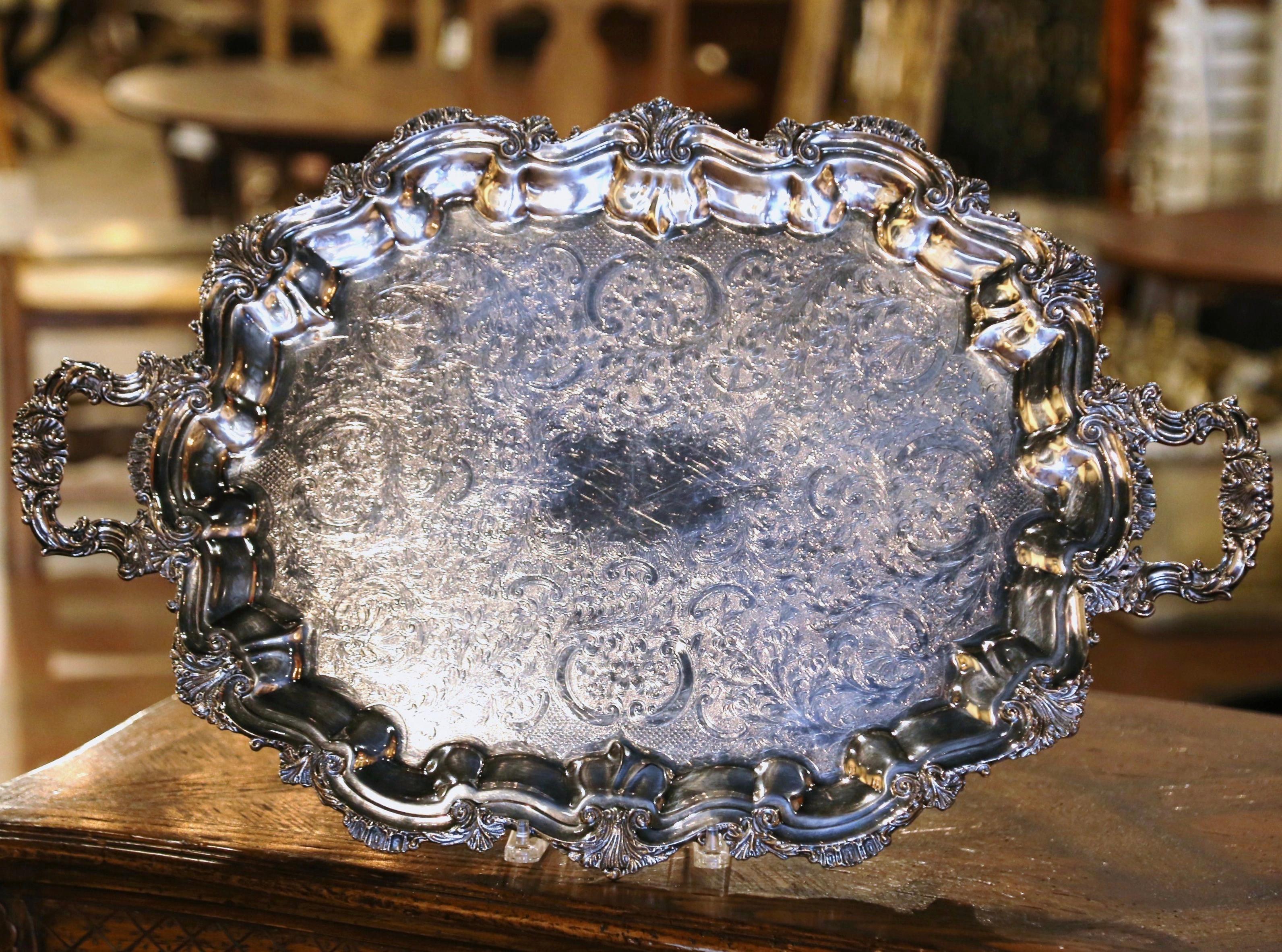 Serve food in style on this elegant antique tray. Crafted in France circa 1950, the decorative tray sits on four curved feet decorated with shell motifs, and features ornate handles on the sides, elaborate scalloped scrolls around the perimeter and