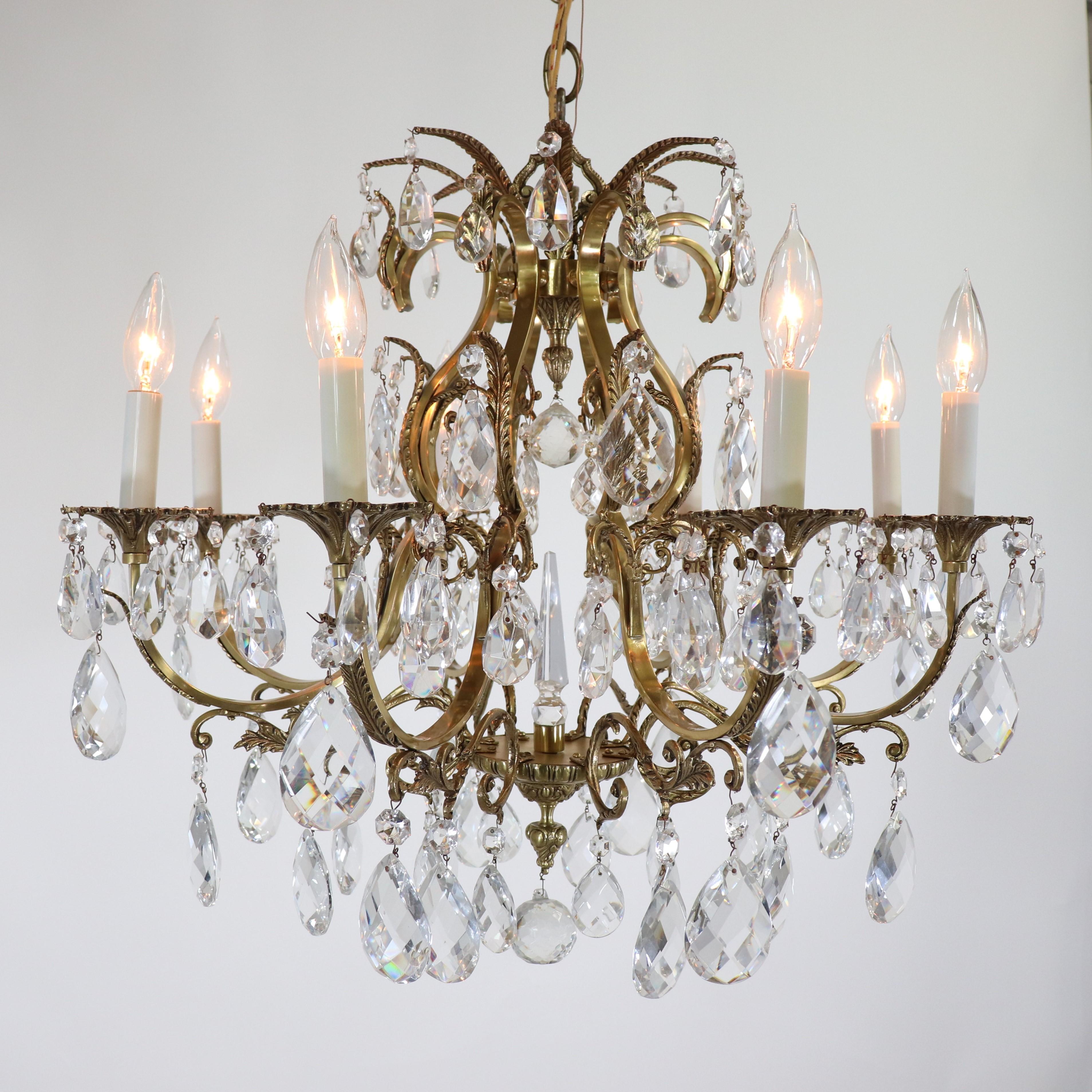 A mid-century Louis XV-style brass and crystal chandelier with bronze acanthus mounts on scroll arms forming a curvaceous birdcage frame. The chandelier is draped with classic teardrop etched crystal pendeloques and features a center crystal spear