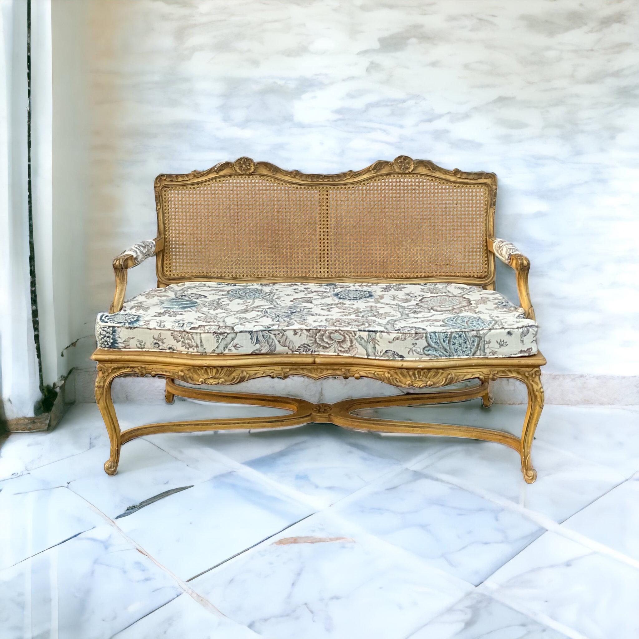 This is a mid-century French Louis XV style caned settee with an antique ivory finish. The linen cushion is new and in neutral florals.